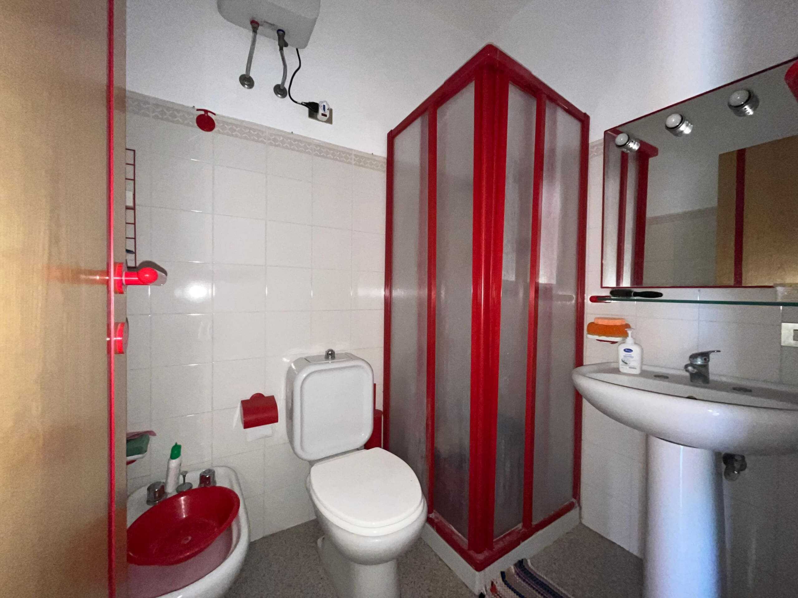 Box doccia rosso con rivestimento in vetro in un bagno moderno NextCasa. Arredo bagno funzionale con sanitari bianchi e accessori coordinati, ideale per soluzioni abitative di alta qualità.