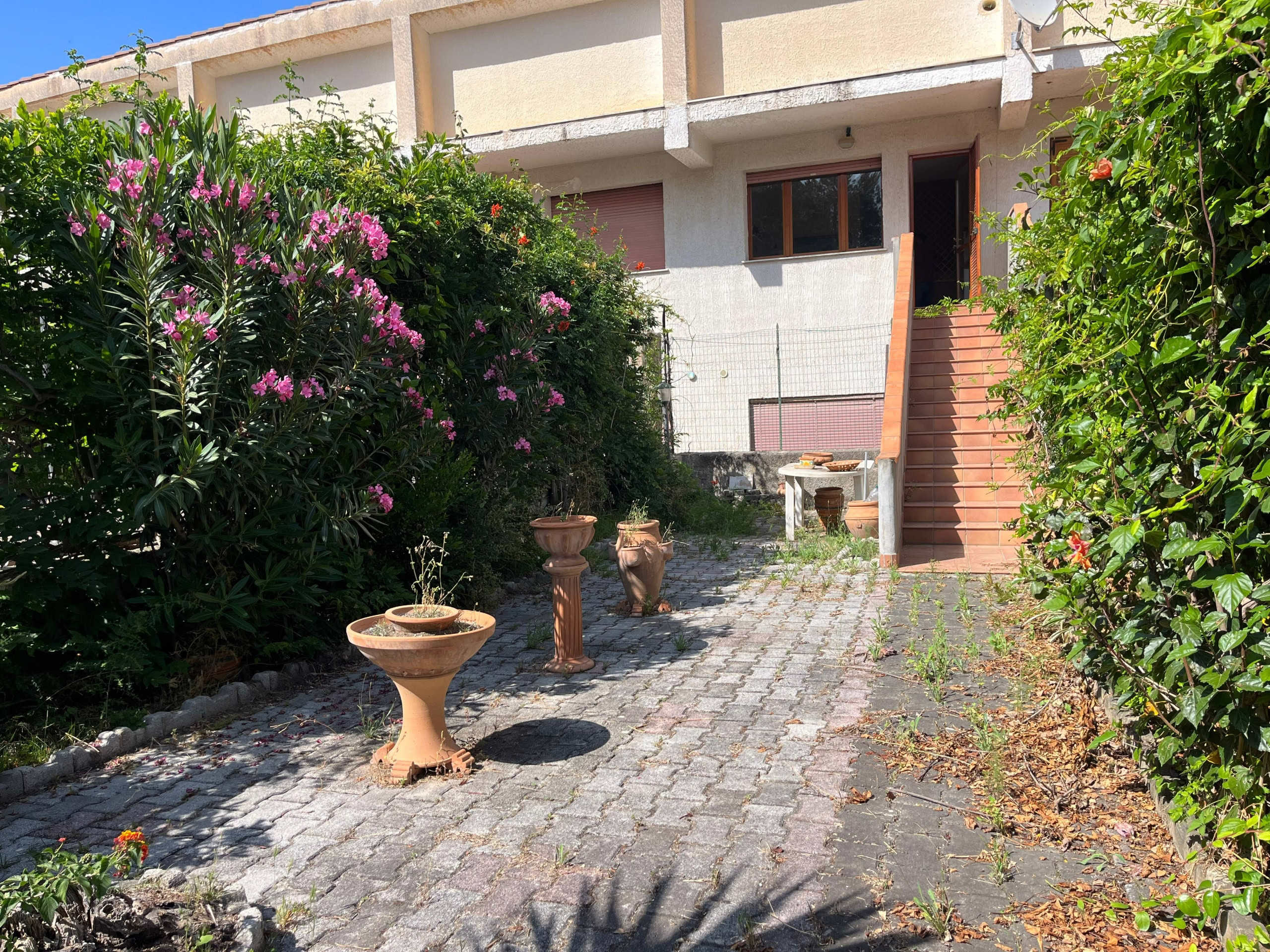 Giardino esterno con vaso di fiori, strada in pietra, scale in terracotta e vivienda moderna con balcone, zona residenziale, giardino ben curato, stile italiano, NextCasa Immobiliare.