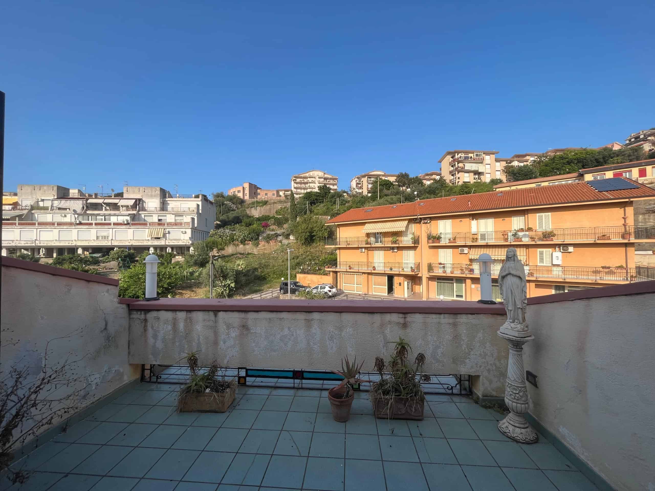 Balcone con vista su quartiere residenziale, appartamenti e case in collina, illuminato dal sole, con piante e scultura religiosa, ideale per chi cerca immobili in vendita o affitto a Napoli e dintorni.
