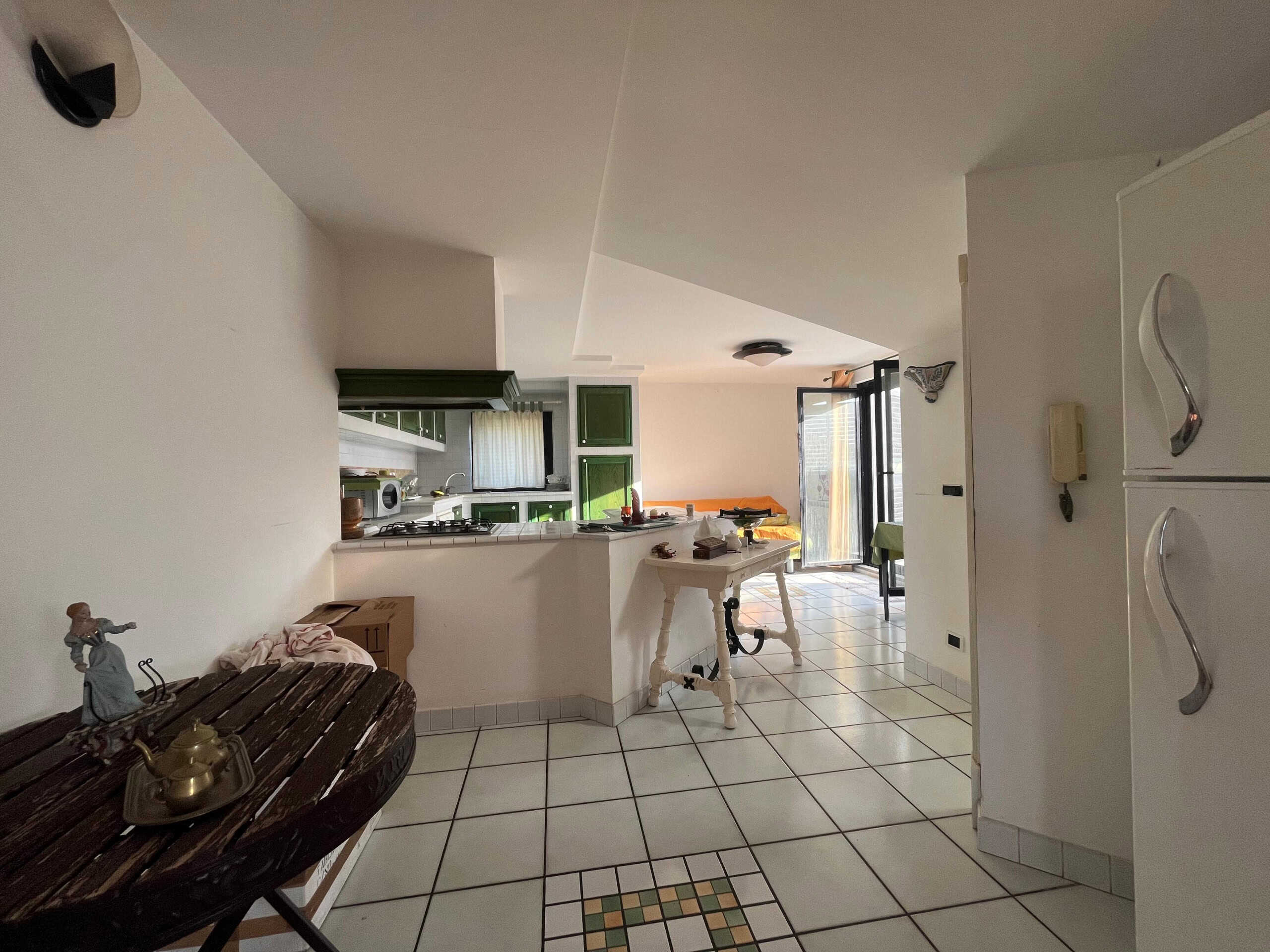 Lavanderia e cucina open space con mobili verdi, cucina a vista e zona living con balcone soleggiato, arredamento funzionale e stile semplice, perfetta soluzione abitativa a NextCasa.