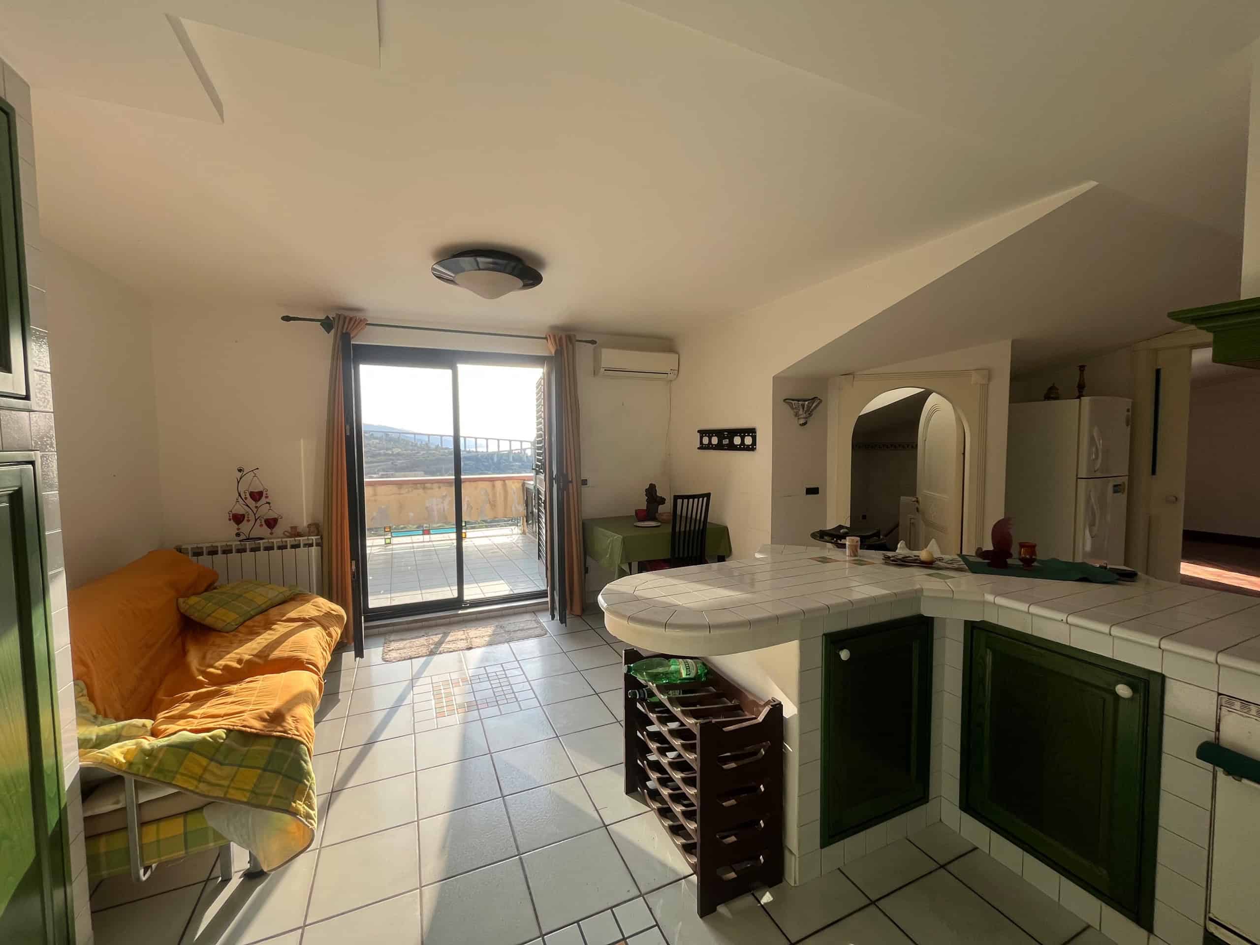 Luminoso soggiorno con balcone vista mare, arredamento pratico, cucina a vista con tavolo da pranzo, ideale per case vacanza o immobili in affitto a lungo termine a NextCasa.