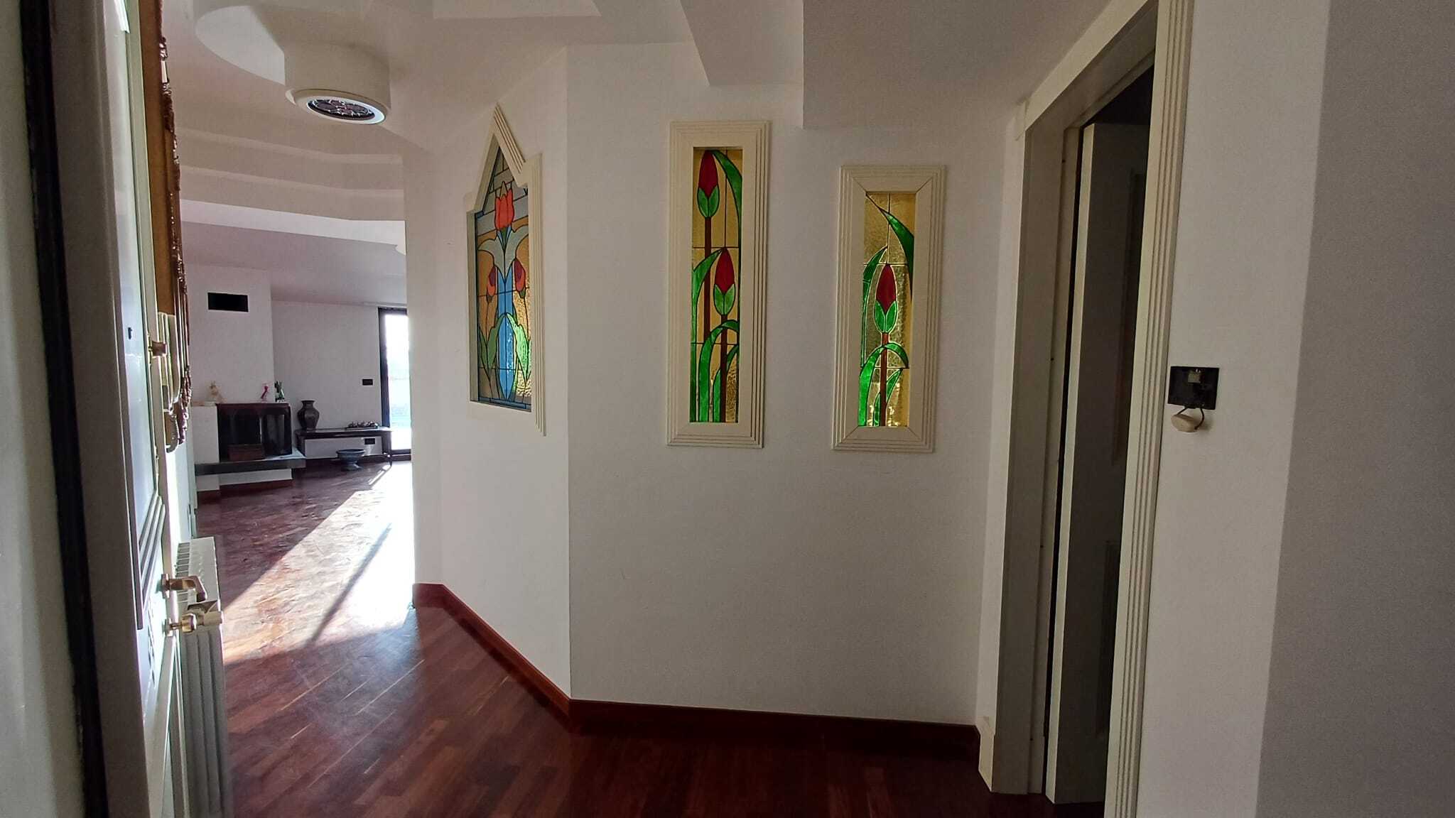 Vetrate decorative in stile Tiffany con motivi floreali in una casa moderna, illuminano un ingresso elegante con pareti bianche e pavimenti in legno pregiato.