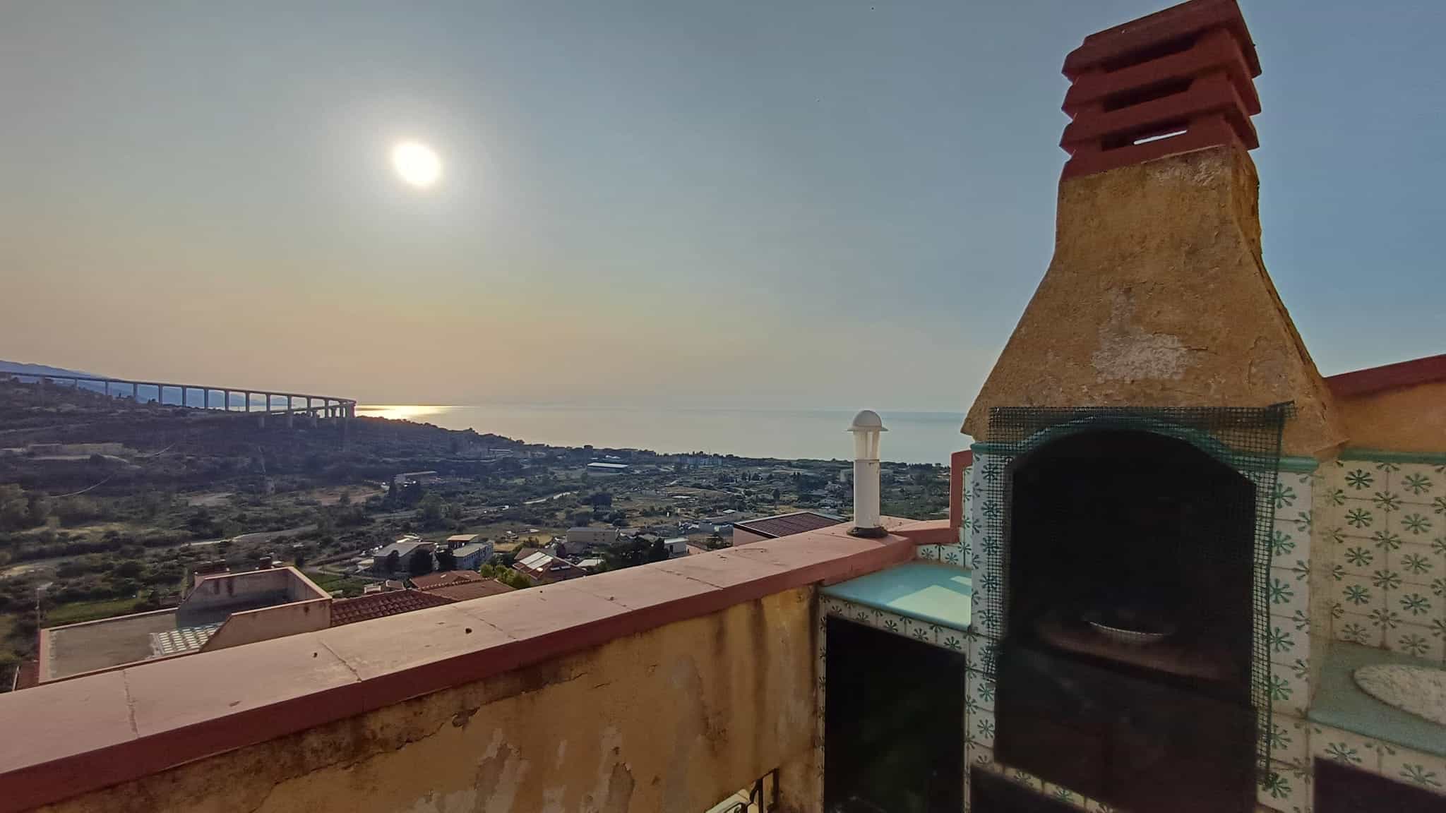 Fronte terrazza vista mare con barbecue in stile mediterraneo, cielo sereno, luce calda al tramonto, paesaggio collinare e vista sulla costa, atmosfera rilassante e accogliente.