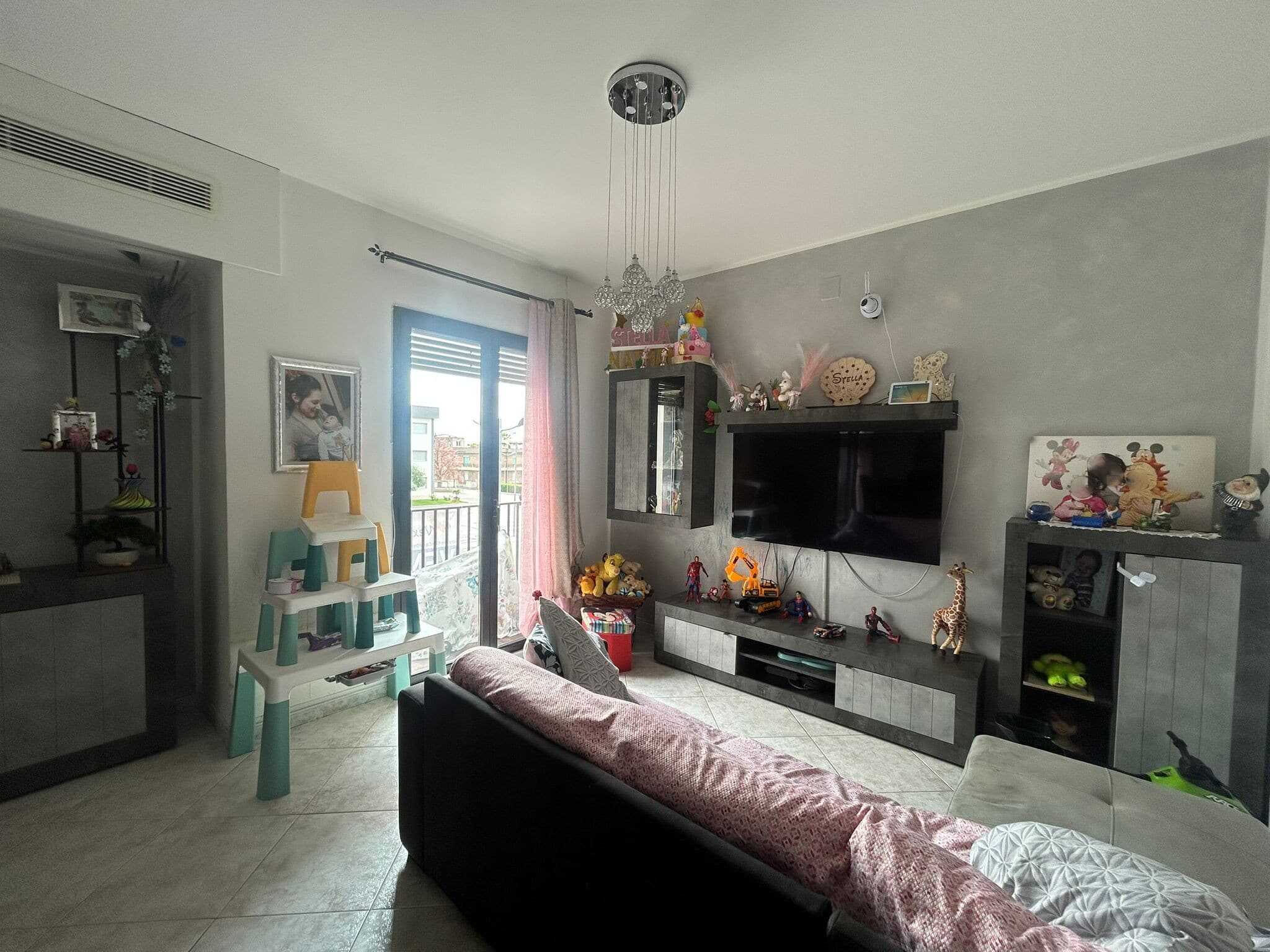 Tecnologia smart e arredi moderni in soggiorno luminoso con parete attrezzata e area giochi bambini, balcone con vista, ideale per vivere in famiglia.