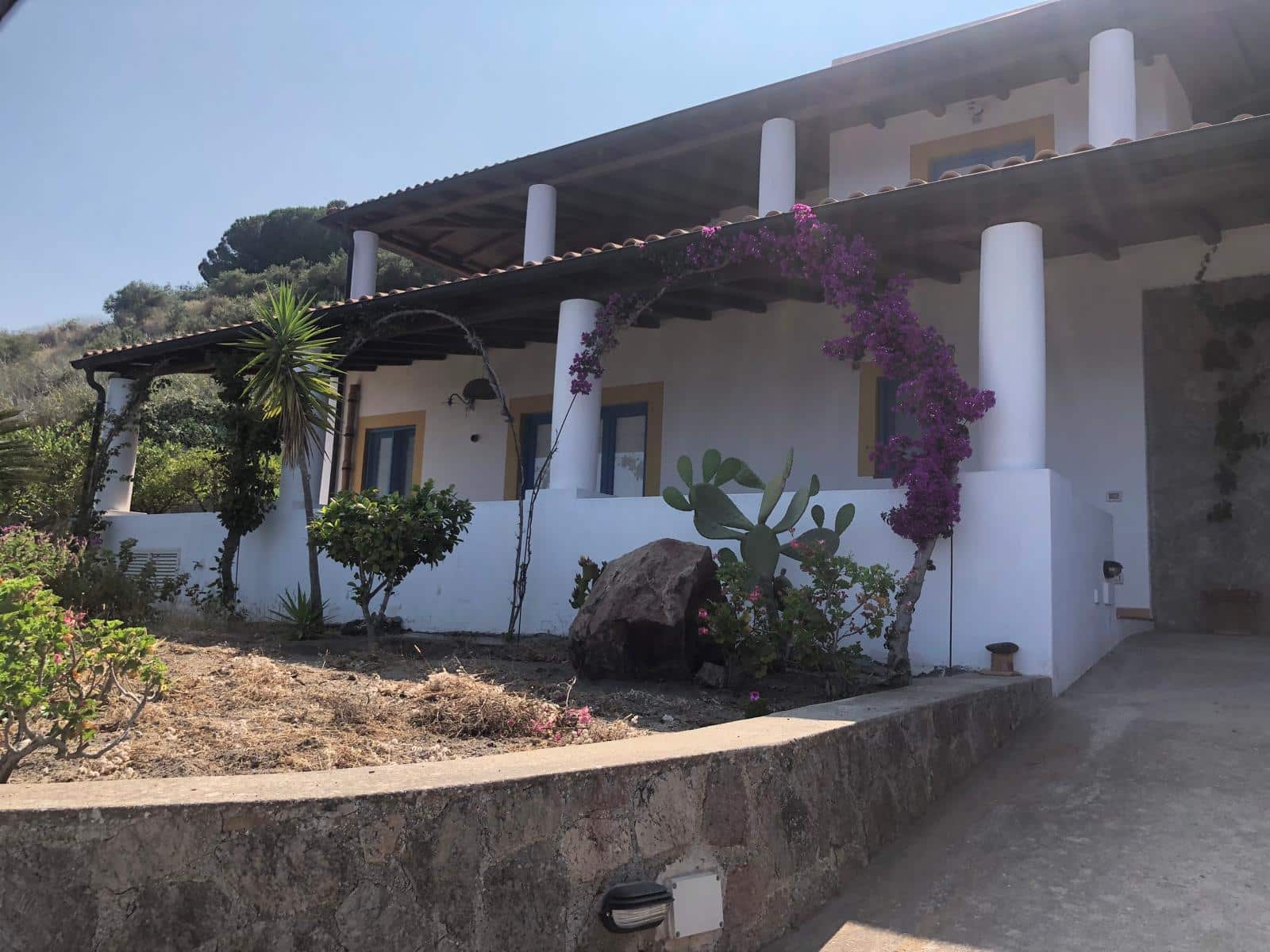 Villa panoramica con giardino curato, piante tropicali e fiori colorati, immersa nella natura, ideale per case vacanza in Toscana o Sicilia. Architettura tradizionale con stile mediterraneo, vista mozzafiato, relax e privacy assicurati.