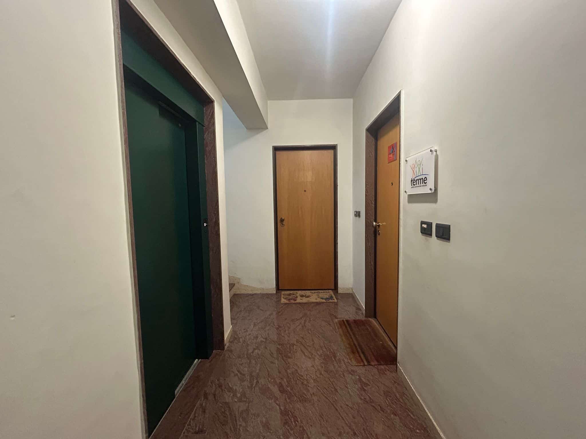 Elevatore e porte di accesso condominiali in un edificio residenziale con pavimento in marmo.