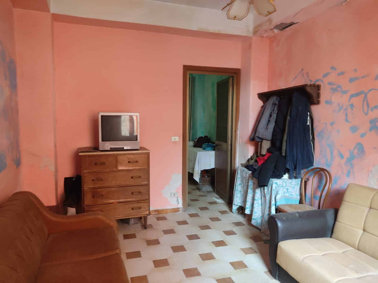 Vecchio soggiorno con pareti rosa, mobili in legno, divani vintage e television a tubo catodico, ambiente da ristrutturare con pareti danneggiate e arredamento datato, ideale per progetto di rinnovamento casa.