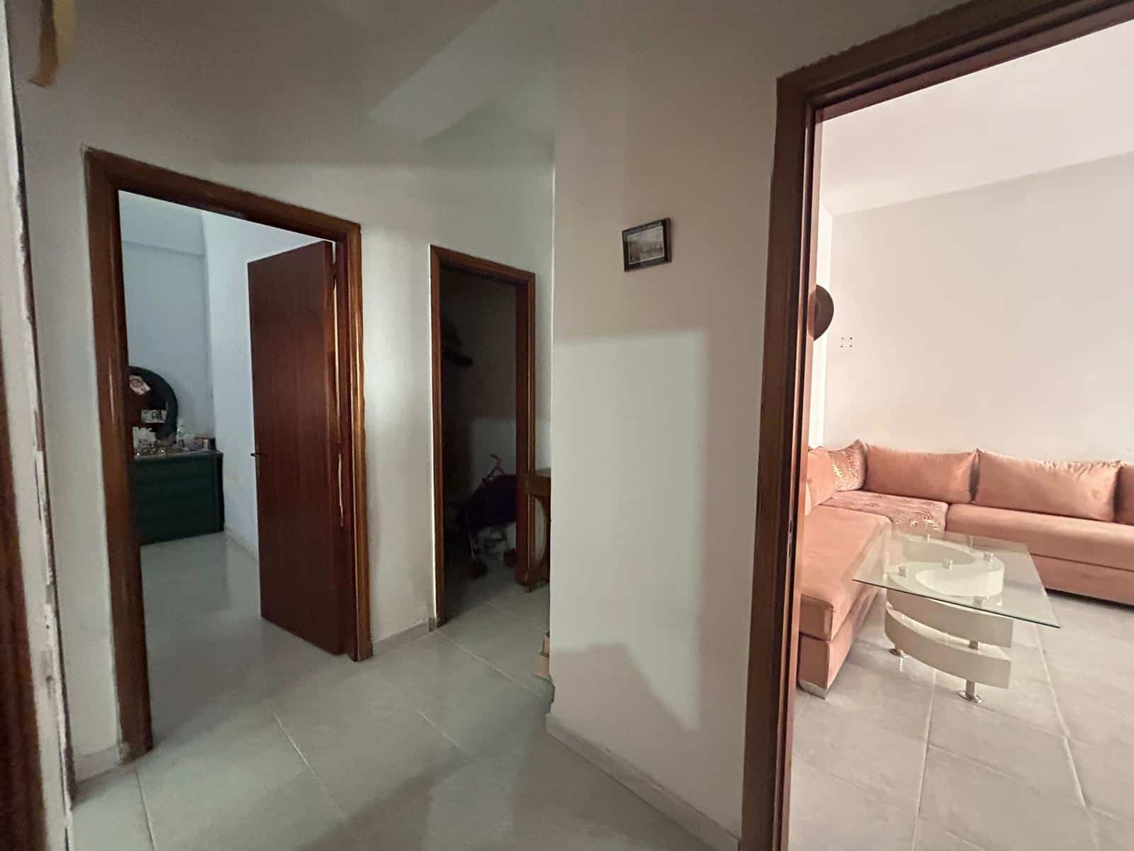 Immagine di un ingresso con porte in legno e soggiorno visibile attraverso la porta aperta, arredato con divano beige e tavolino in vetro, in un appartamento moderno e luminoso.