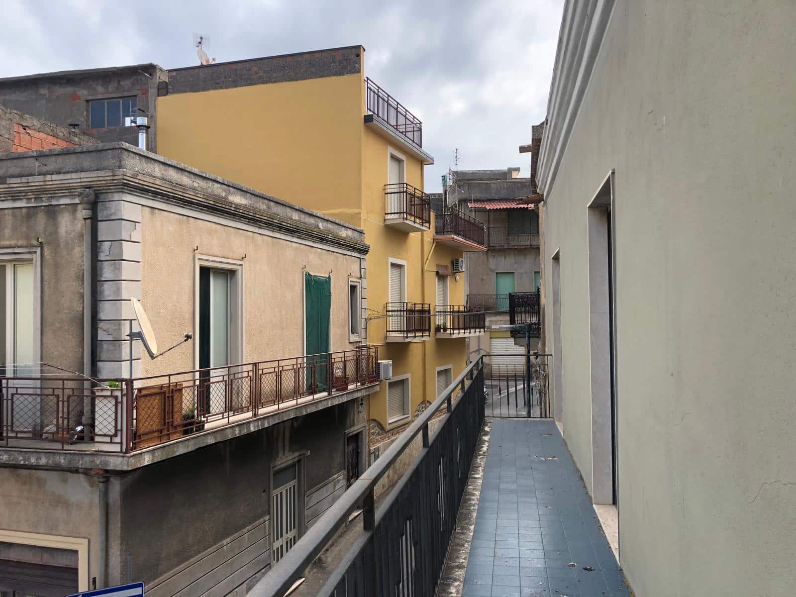 Balcone di un edificio residenziale in centro città con viste sulle facciate di altri edifici limitrofi, balconi con grate di ferro e dettagli architettonici in un contesto urbano.