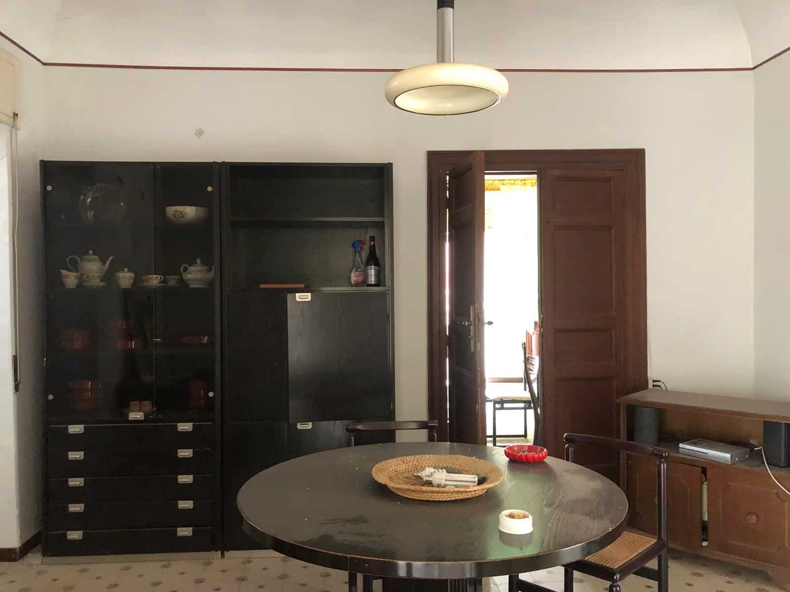 Elegante zona pranzo in casa storica con arredi in stile vintage, tavolo rotondo e mobili in legno, ambiente luminoso con porta di design, perfetto per vivere momenti conviviali e valorizzare l'ambiente abitativo.