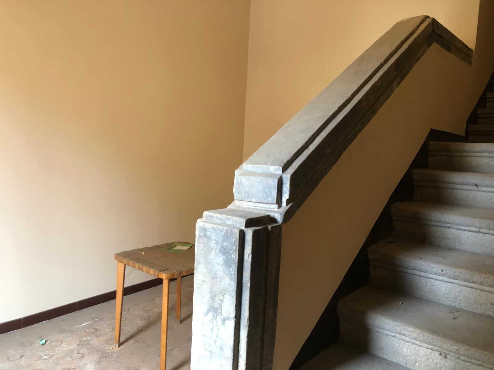Scale in pietra antico, spazio interno di una casa storica o edificio rustico, dettaglio di arredamento semplice e funzionale.