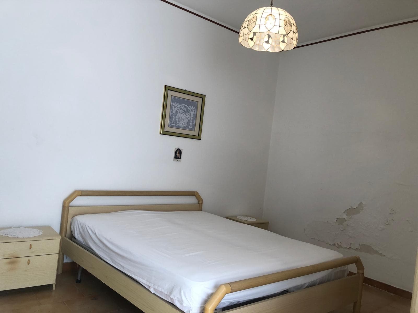 Letto matrimoniale in stile semplice con camino in legno naturale, due comodini coordinati, decorazioni classiche alle pareti, illuminazione complessa, ambiente confortevole e funzionale, ideale per residenze e affitti veloci.