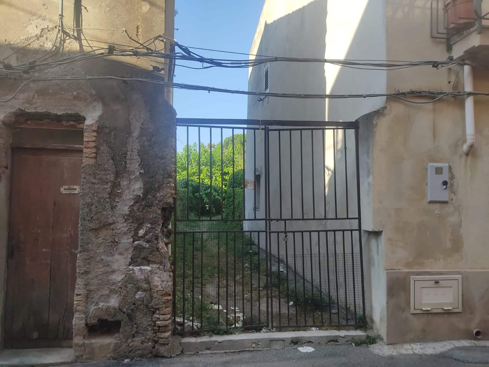 Ferrovia nera che delimita un cancello in metallo tra edifici antichi e moderni, con fili elettrici visibili, in un contesto urbano storico.