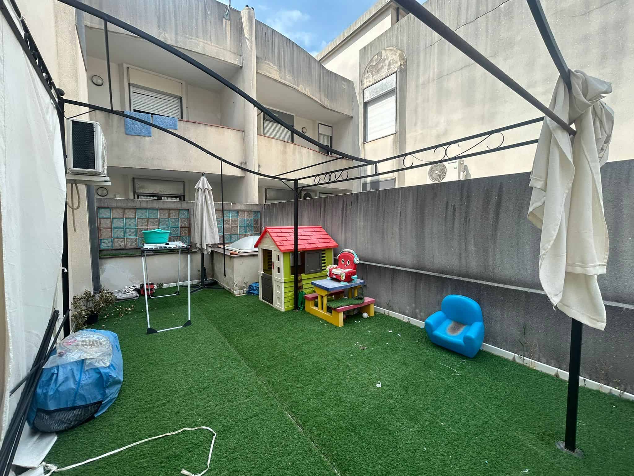 Balcone con area giochi per bambini, tappeto in erba artificiale e zone per il relax all'aperto, ideale per ambienti residenziali e spazi esterni funzionali.