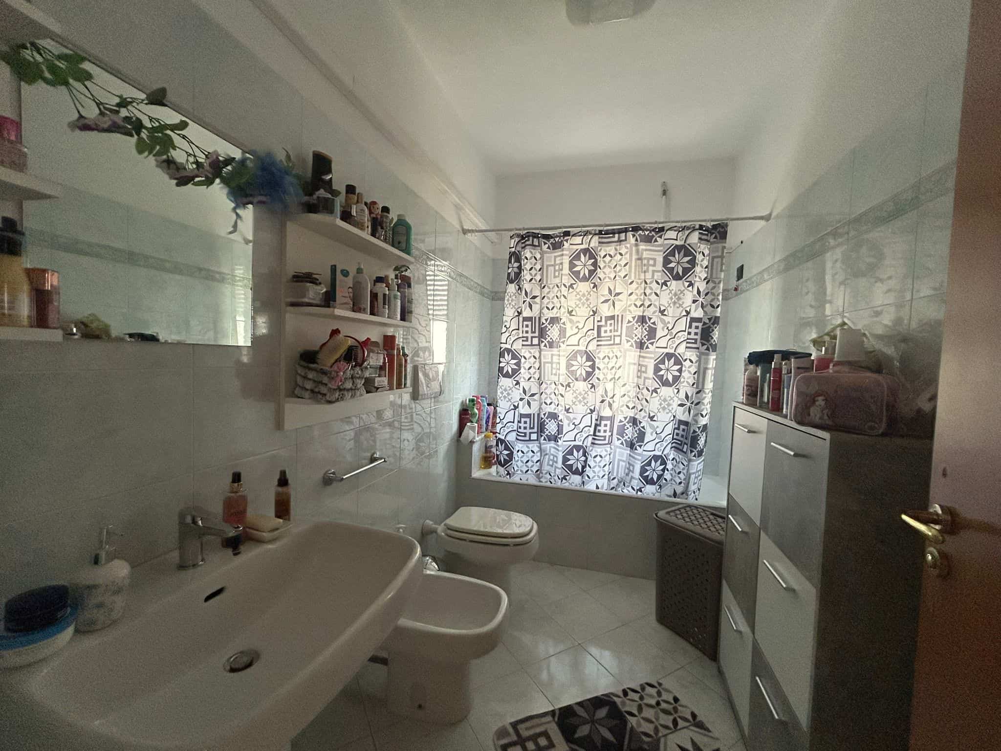 Lavabo e servizi igienici in un appartamento residenziale con arredi funzionali e una finestra con tendina decorativa, ambiente luminoso e pratico, ideale per uso quotidiano in zona abitativa.