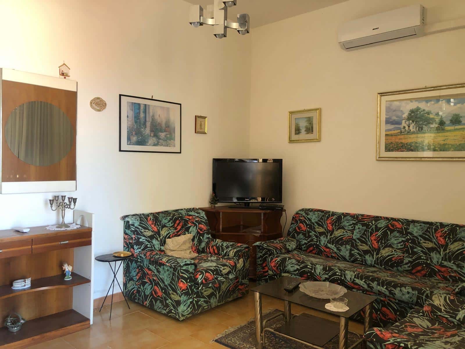 Soggiorno con divani, televisore, decorazioni artistiche e mobili in stile classico, ambiente accogliente e arredato con cura, ideale per la casa e il relax.