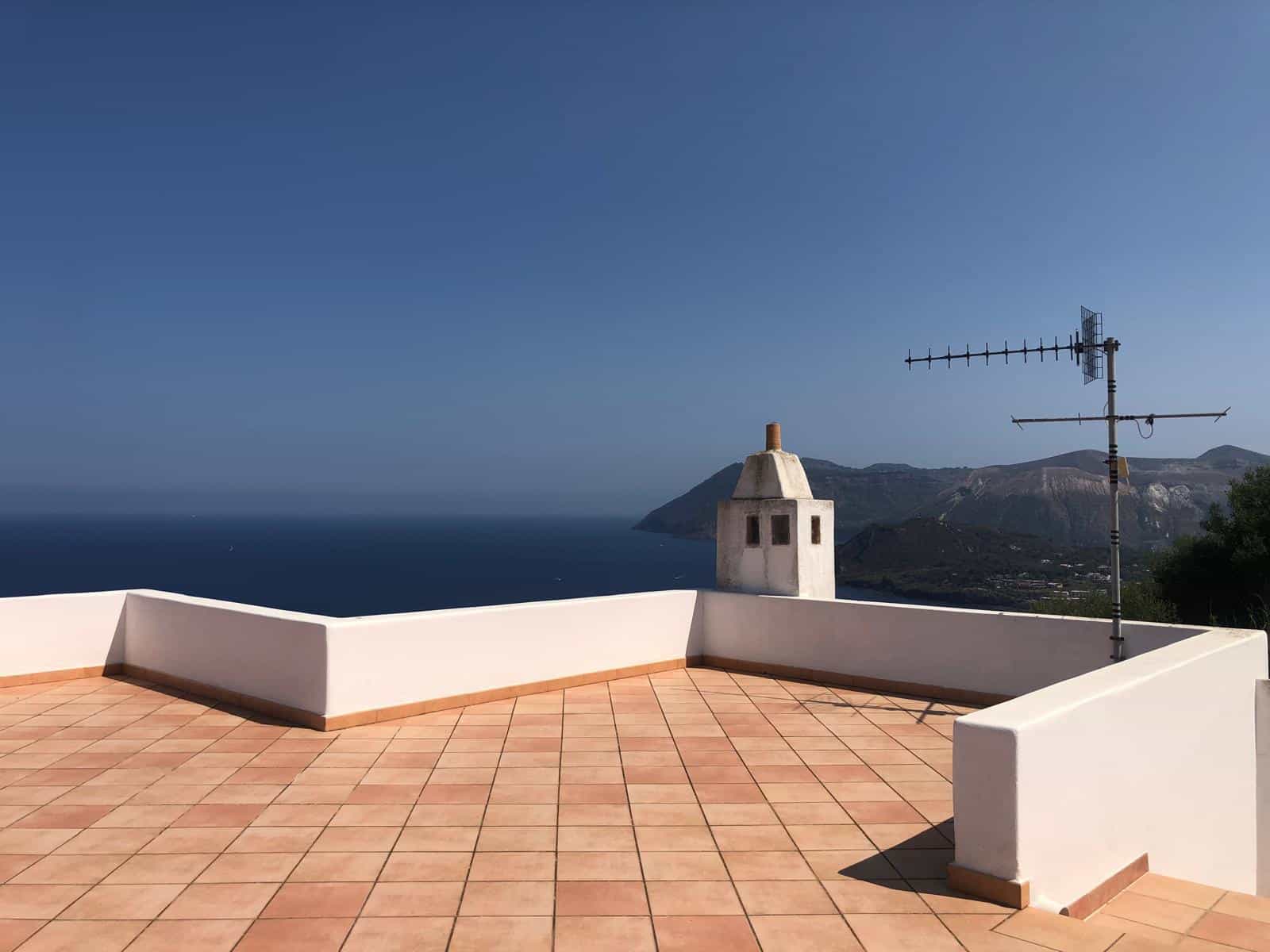 Balcone panoramico con vista sul mare e sulle montagne, pavimento in gres effetto terracotta, lavabo in pietra e antenna TV, ideale per case vacanza e proprietà di lusso in affitto o vendita.