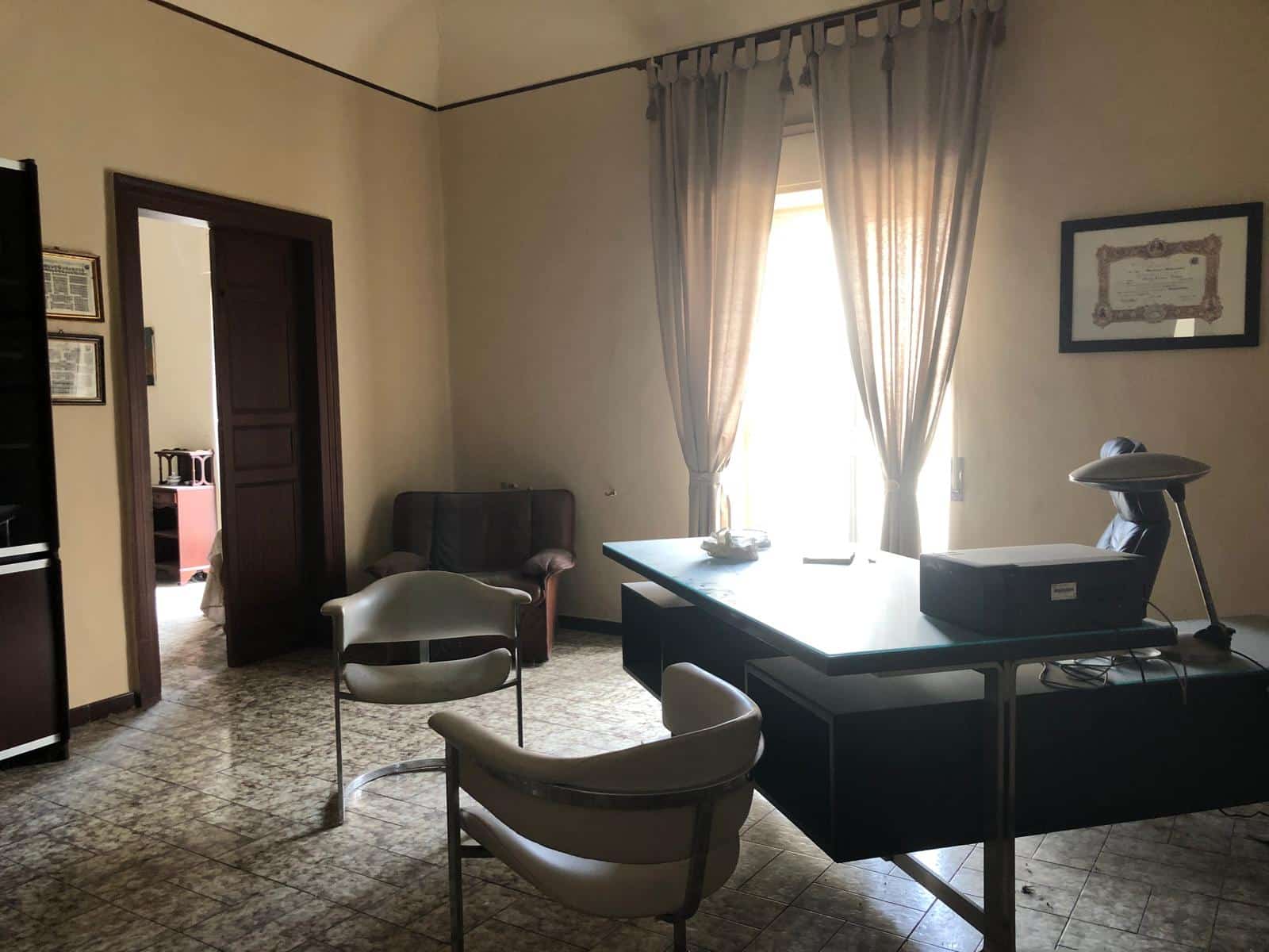 Stanza ufficio con scrivania, sedia, poltrona e finestra luminosa con tende beige, ambiente professionale e accogliente.