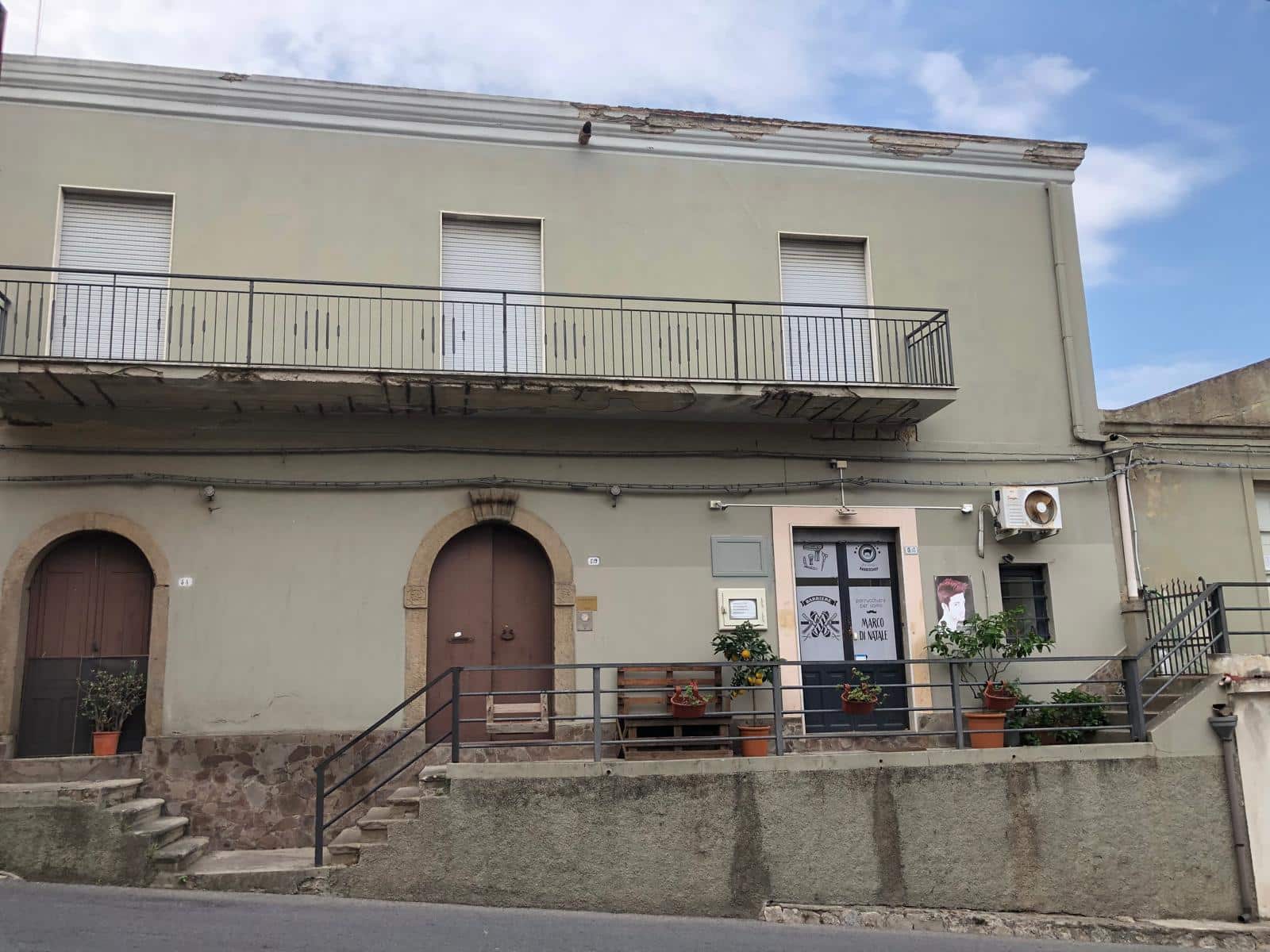Casa indipendente con balcone e porta d'ingresso in stile classico, situata in zona urbana, con terrazza e piante decorative. Facciata in tonalità neutra, perfetta per investimento immobiliare.