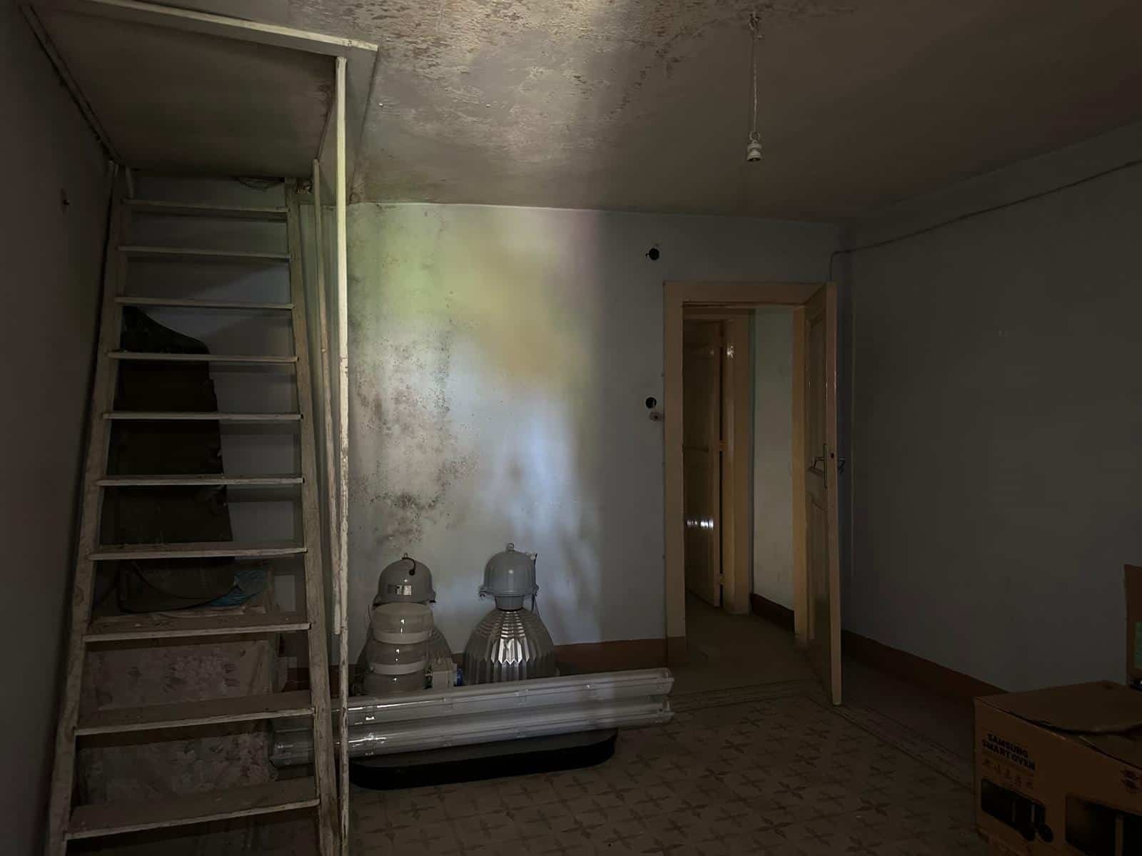 Luce naturale in una stanza in fase di ristrutturazione, con scaffale in legno, lampade da soffitto da installare e pareti in fase di verniciatura, esempio di lavori di ristrutturazione edilizia e pronto intervento casa.