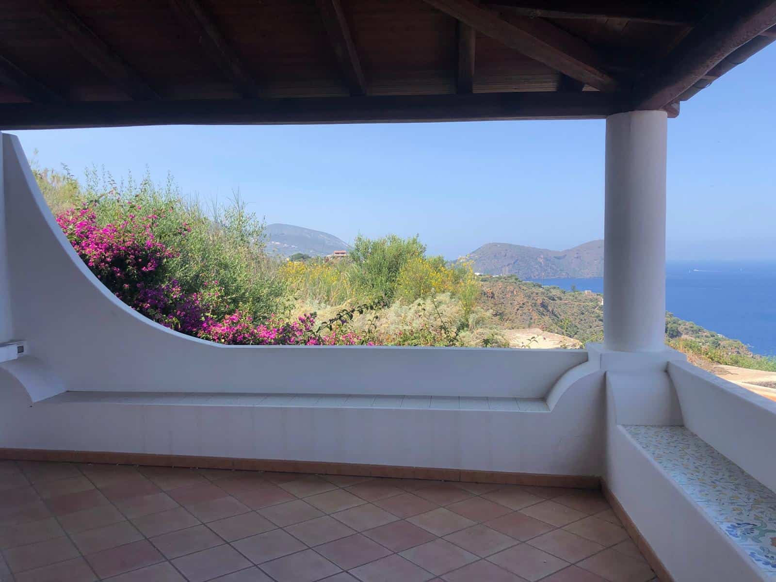 Balcone con vista panoramica sul mare e sulle colline, con decorazioni mediterranee e piante colorate, perfetto per relax e momenti di convivialità in ambienti naturali.