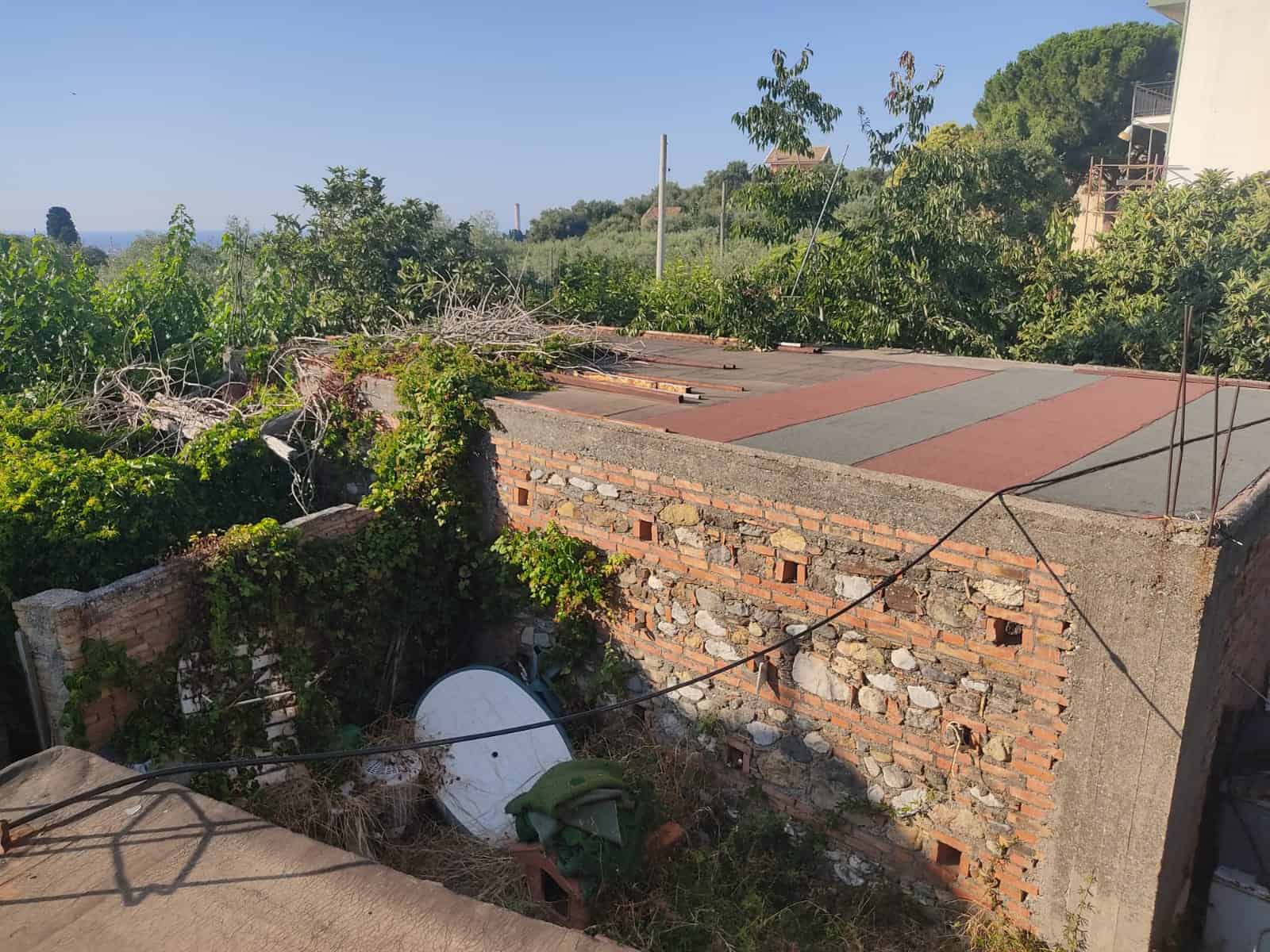 Tetto di una casa in fase di ristrutturazione con mattoni a vista, circondata da vegetazione verde e spazio aperto, ideale per investimenti immobiliari con NextCasa.