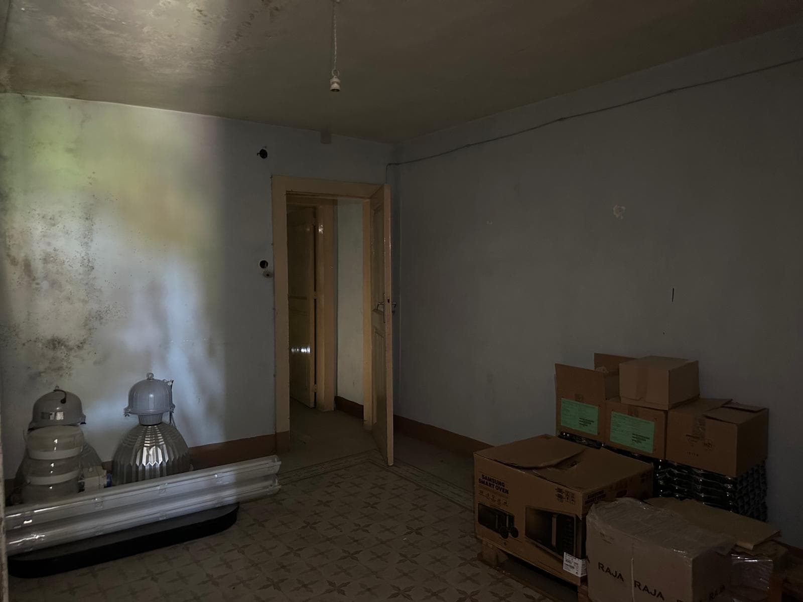 Parete interna di una casa in ristrutturazione con scatole di imballaggio e materiali da costruzione, ambiente in fase di rinnovamento con pareti spoglie e pavimento decorato in stile classico.
