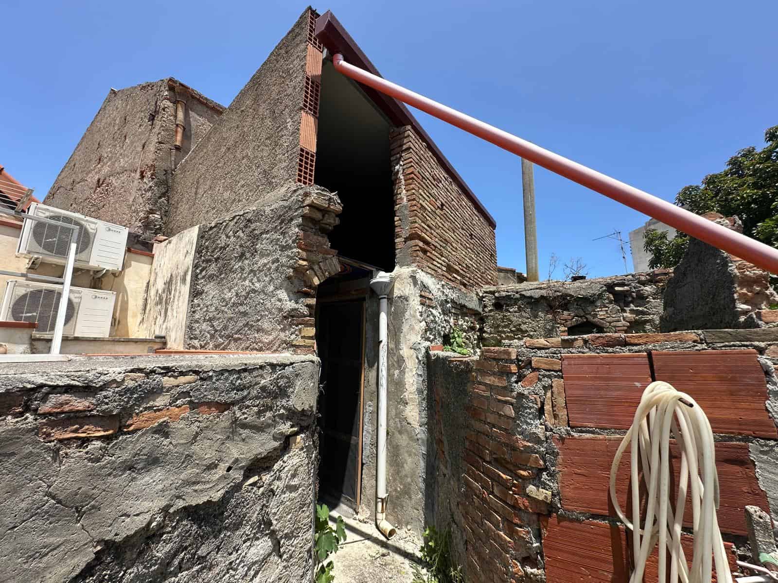 Vecchio stabile in corso di ristrutturazione con muri in pietra e mattoni, presenza di tubi e aria condizionata, vicino a costruzioni moderne, in zona urbana, sotto il cielo azzurro.