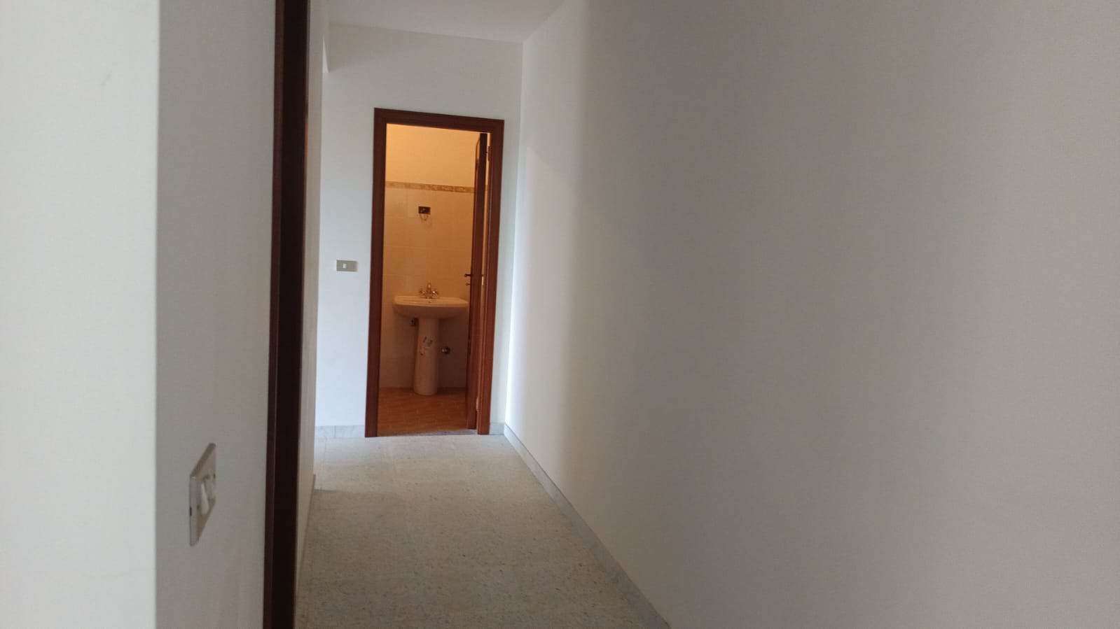 Spazio vuoto in corridoio con porta verso bagno con lavabo, ambienti residenziali moderni e luminosi, ideale per immagini di appartamenti in vendita o affitto.