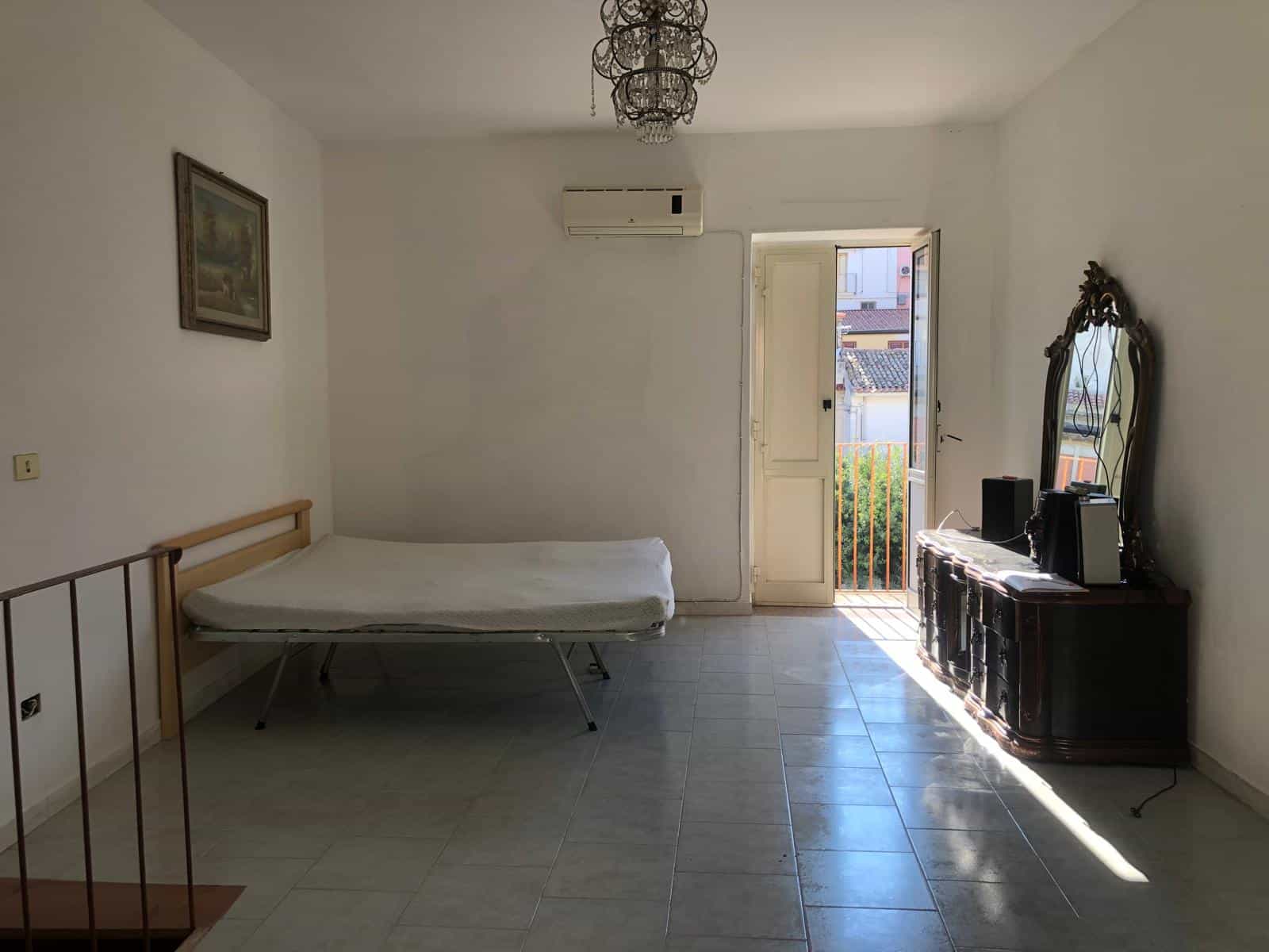 Letto singolo in soggiorno con accesso a balcone, arredi essenziali, ambiente luminoso e spazioso, ideale per affitti temporanei o residenziali, con aria condizionata.
