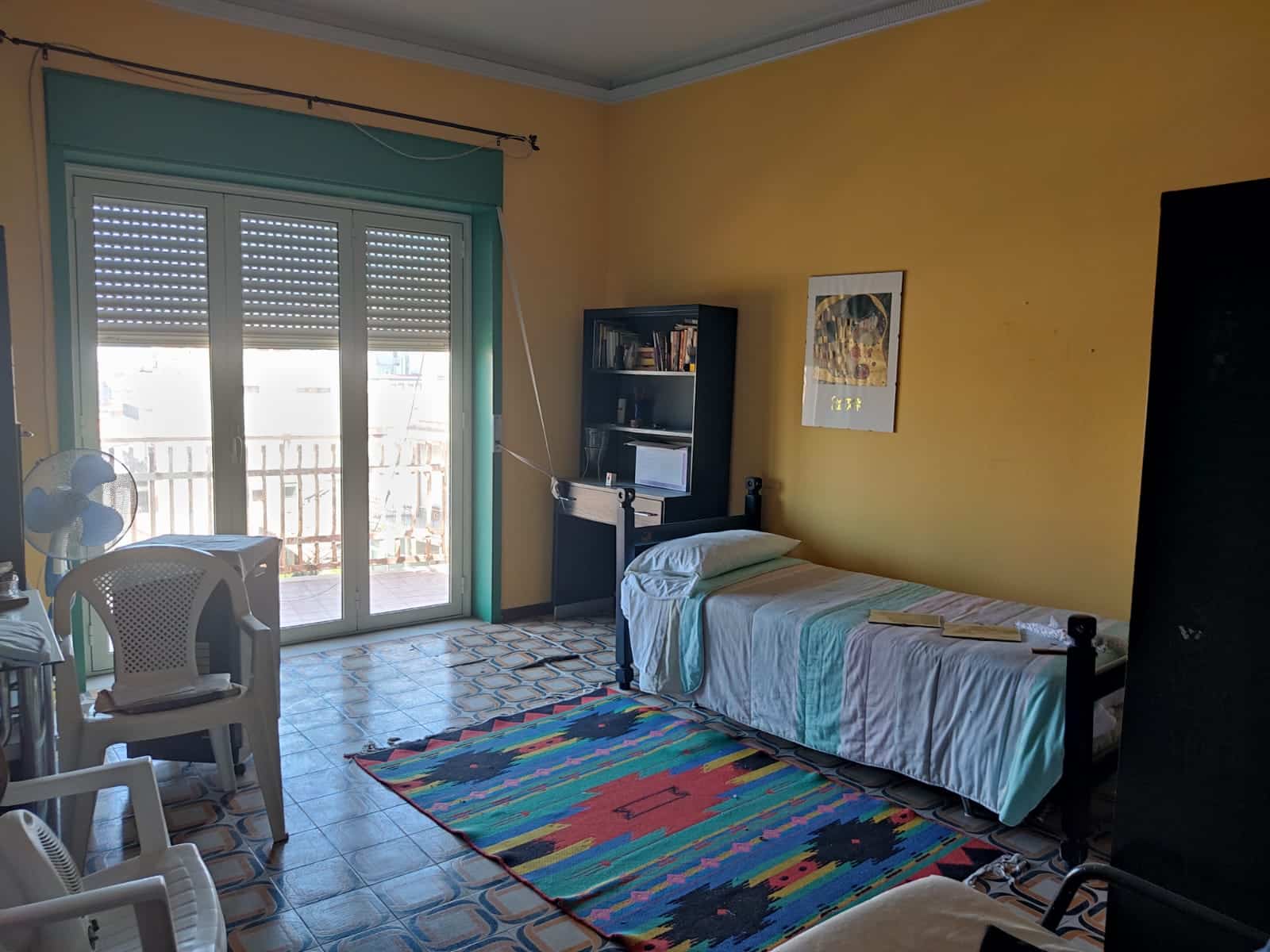Letto singolo in camera con aria condizionata, soggiorno a Milano con mobili in stile semplice, ideale per affitto breve o uso personale, con accesso a balcone e spazio soggiorno funzionale.
