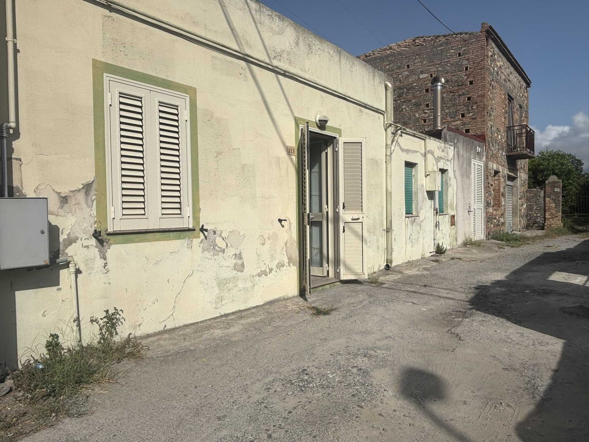 Vecchio edificio residenziale in stile rustico con pareti esterne in pietra e cartongesso, balcone in ferro e finestre con persiane in legno, situato in zona tranquilla.