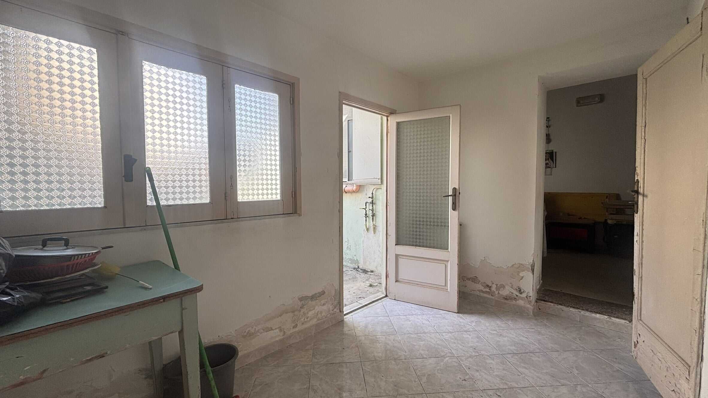 Vecchia casa in affitto con finestre e porta d'ingresso, interni da rinnovare, pareti danneggiate e pavimento in piastrelle, spazio abitativo con potenziale di ristrutturazione e valorizzazione.