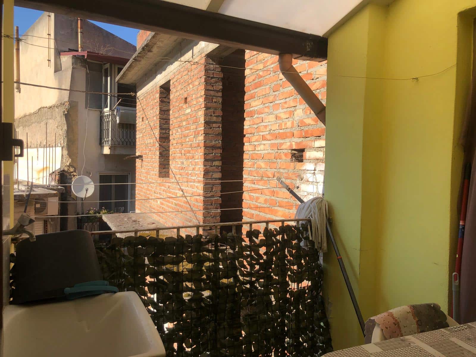 Balcone con muro in mattoni rossi e corda per stendere, vista sulle case vicine con balcone e satellite, in un appartamento urbano.