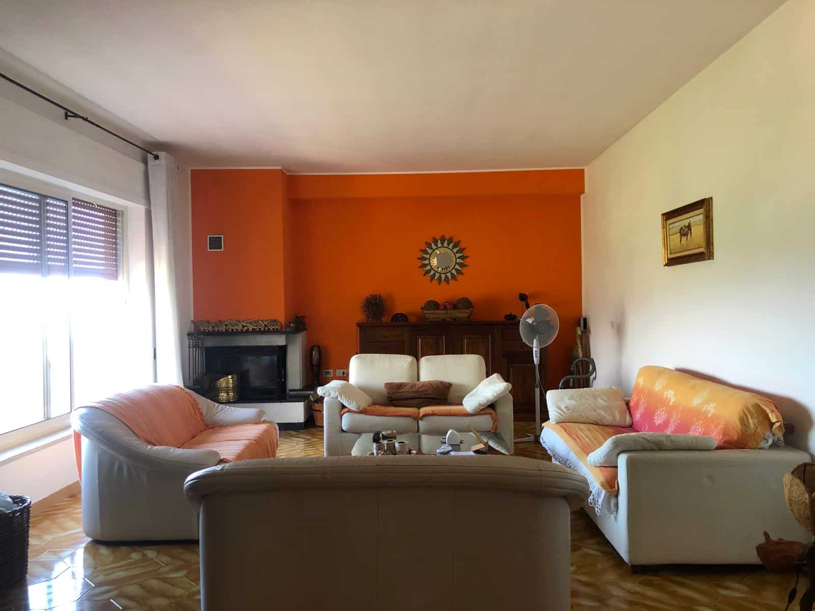 Accogliente soggiorno con divani in pelle e tessuto, camino, pareti colorate in arancione e crema, decorazioni eleganti, ambiente luminoso con ampie finestre e parquet in legno.