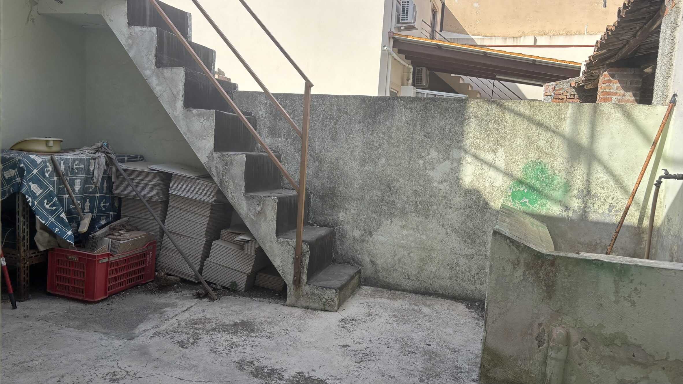 Staircase esterna in cemento con ringhiera in metallo e spazio di deposito con mattonelle e attrezzi da giardinaggio in un cortile condominiale.