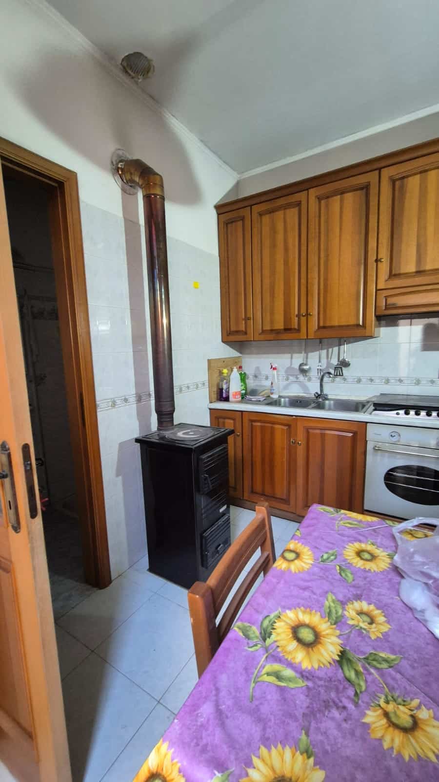 Caldaia a pellet in cucina con camino in ottone, mobili in legno e tavolo con tovaglia fiorata giallo sole.