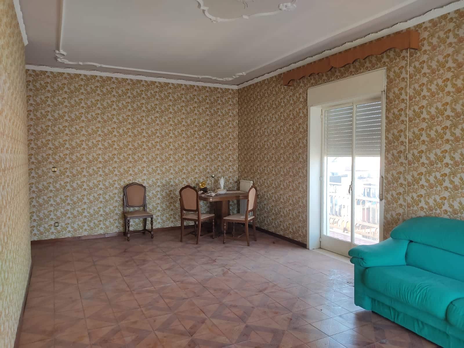 Splendida stanza di soggiorno con pareti rivestite in carta da parati floreale, spaziosa con divano verde e accessori d'epoca, grande finestra con balcone, ideale per immobili residenziali di qualità.