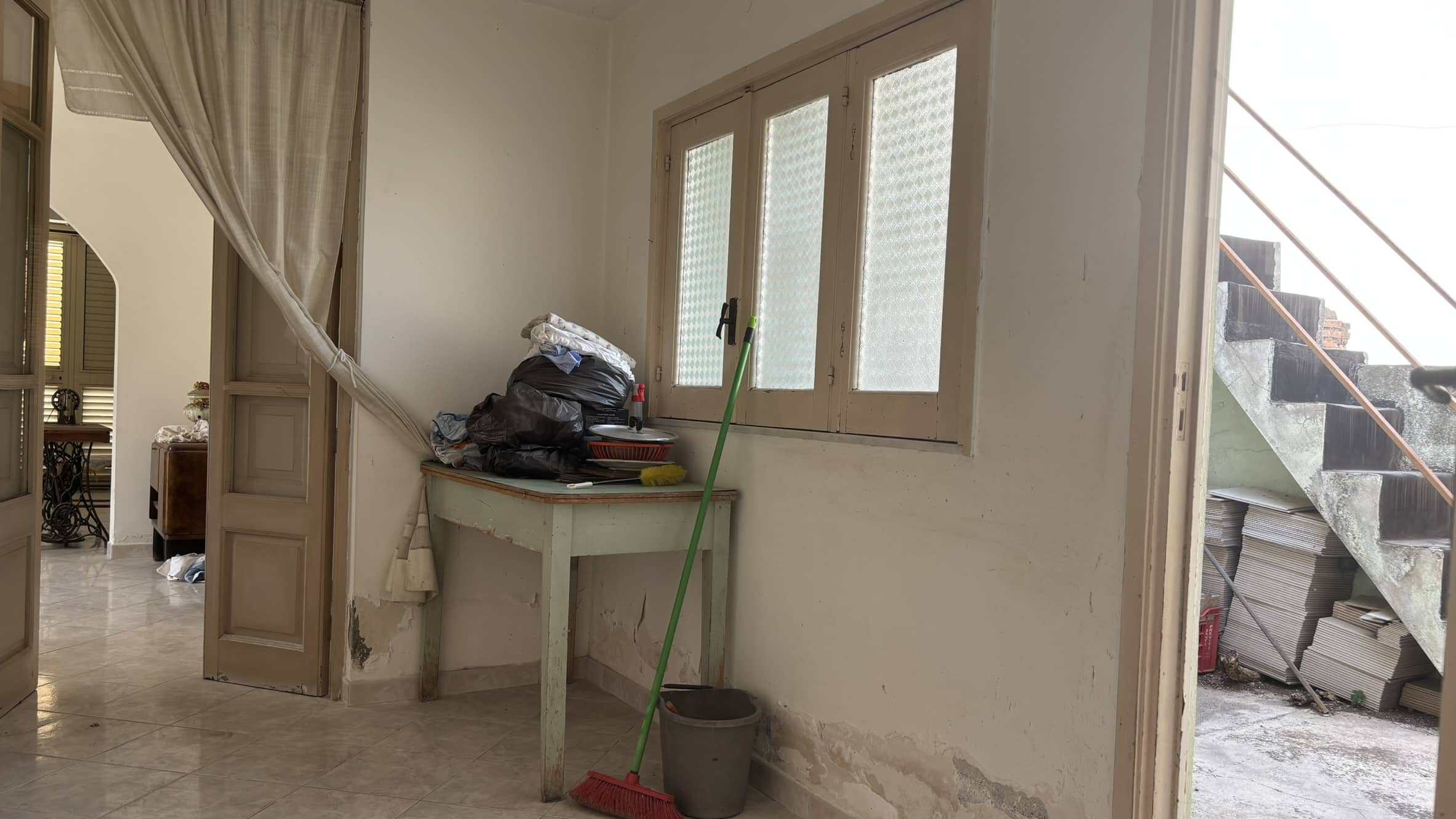 Pulisci casa in corso di ristrutturazione, finestra con persiane, pareti da restaurare, mobili e oggetti vari, scala esterna, pentole e rivestimenti in pietra, ambiente interno con ingresso e accesso al pianerottolo.