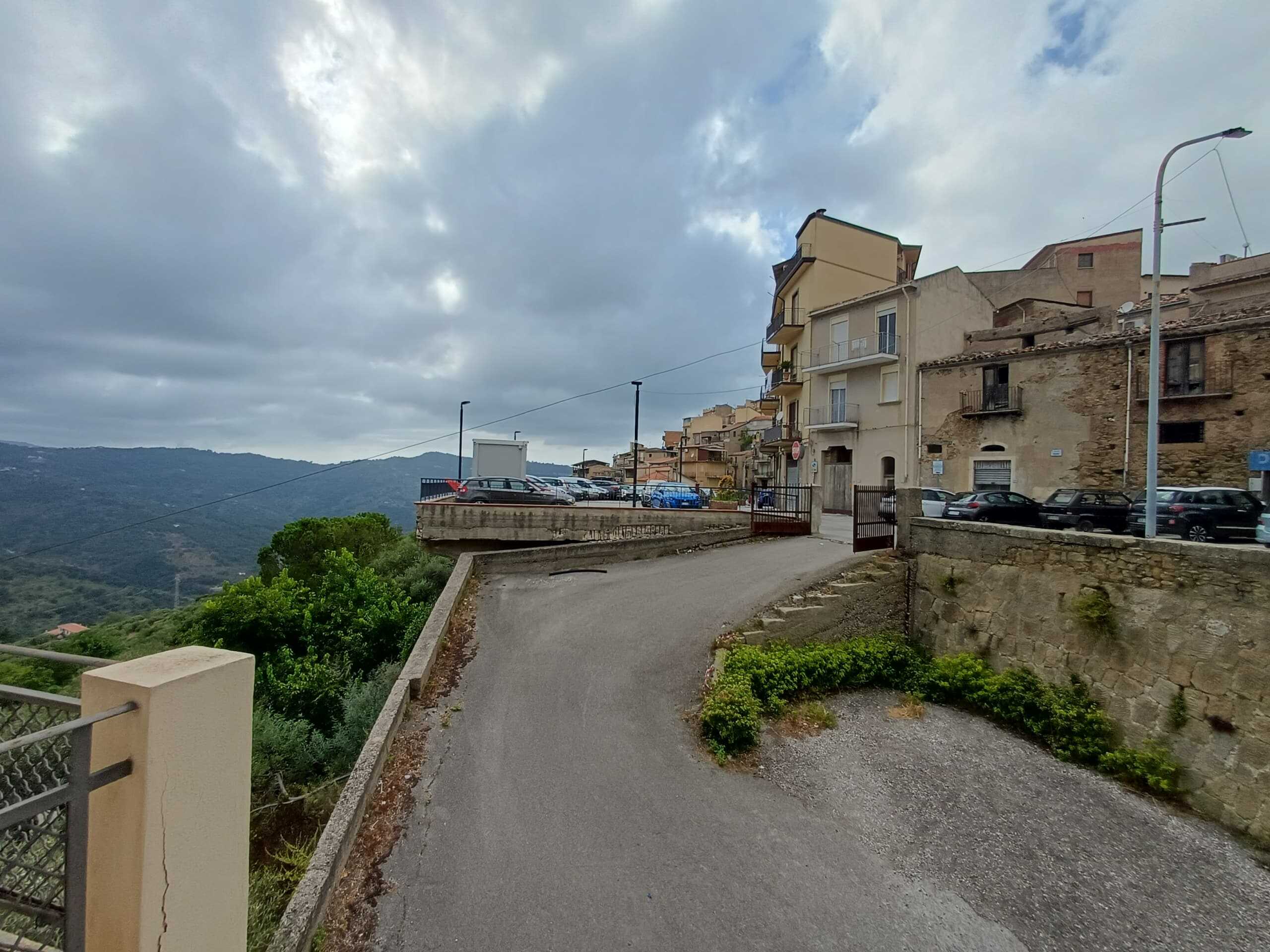 Scorcio di strada in un borgo collinare con edifici storici e vista panoramica sulle montagne sotto un cielo nuvoloso.