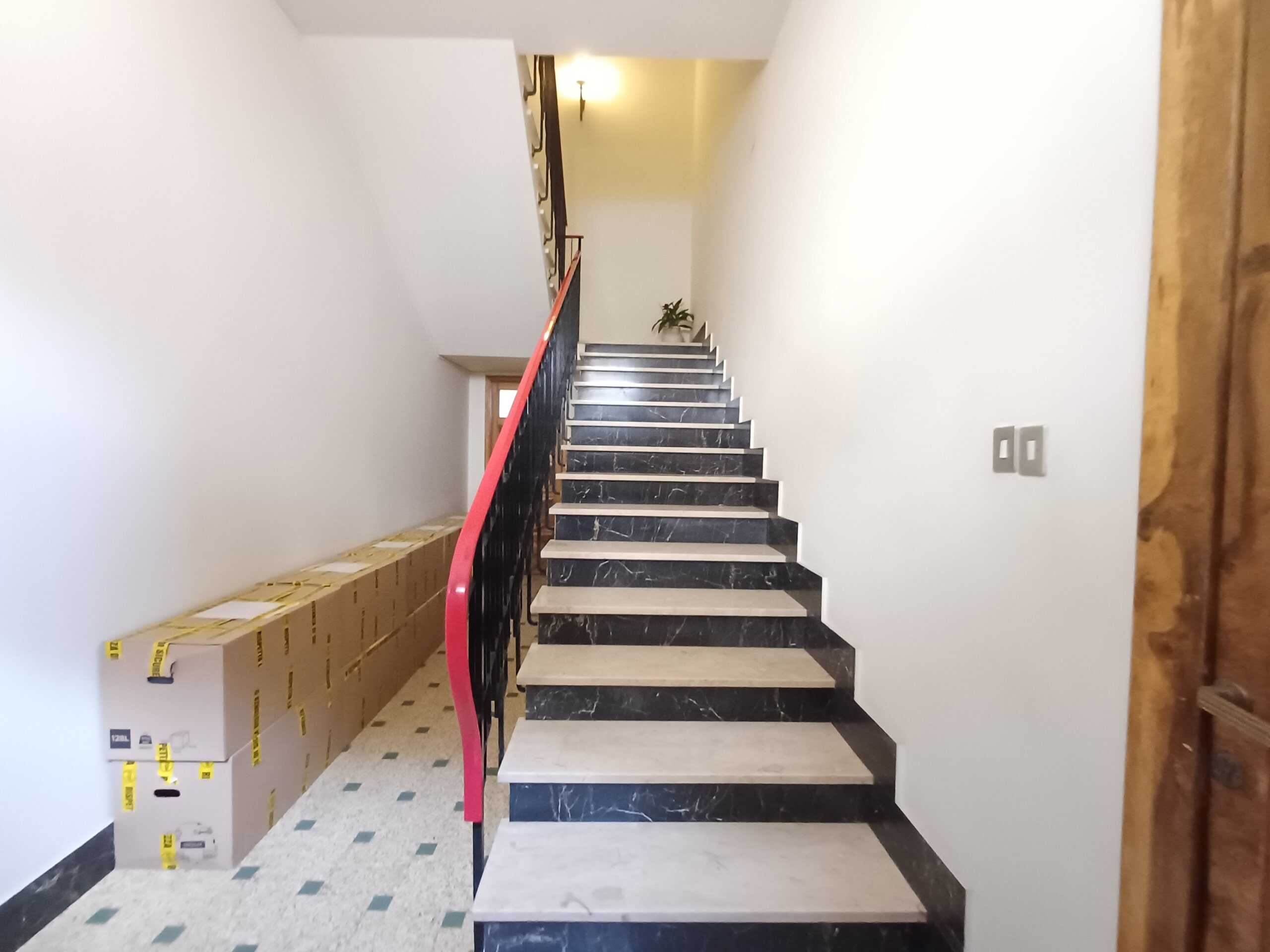 Scale interne in marmo nero e crema, con ringhiera in ferro nera e maniglia rossa, all'interno di un'abitazione moderna, con pareti bianche e spazio Living.