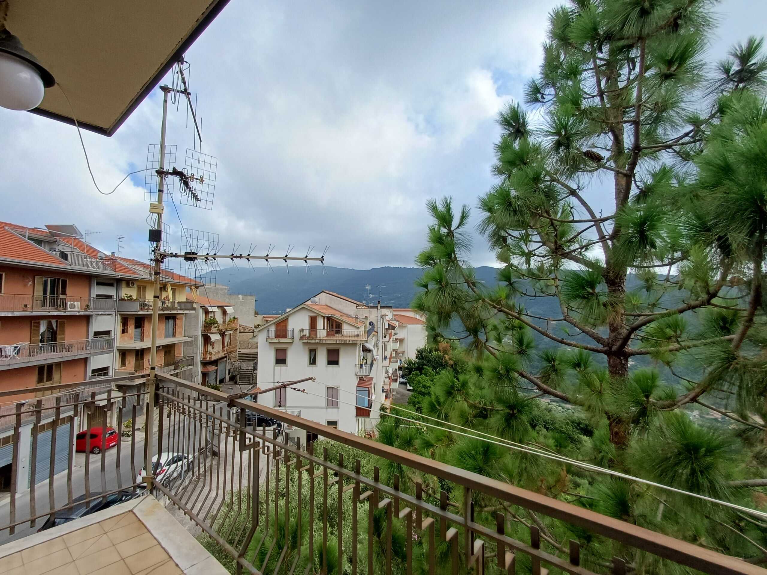 Balcone con vista sucase e natura, in un quartiere residenziale, con tetto in tegole e alberi verdi, perfetto per relax e panorami suggestivi sull'ambiente urbano e naturale.
