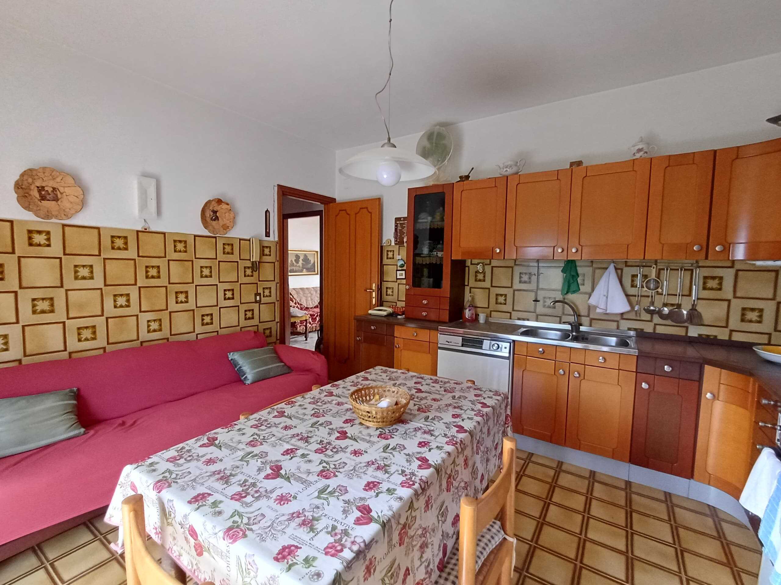 Mobili cucina e soggiorno con pareti rivestite in piastrelle vintage, tavolo da pranzo con tovaglia floreale, divano rosso, armadietti in legno, dettagli retrò, ambiente accogliente e caratteristico.