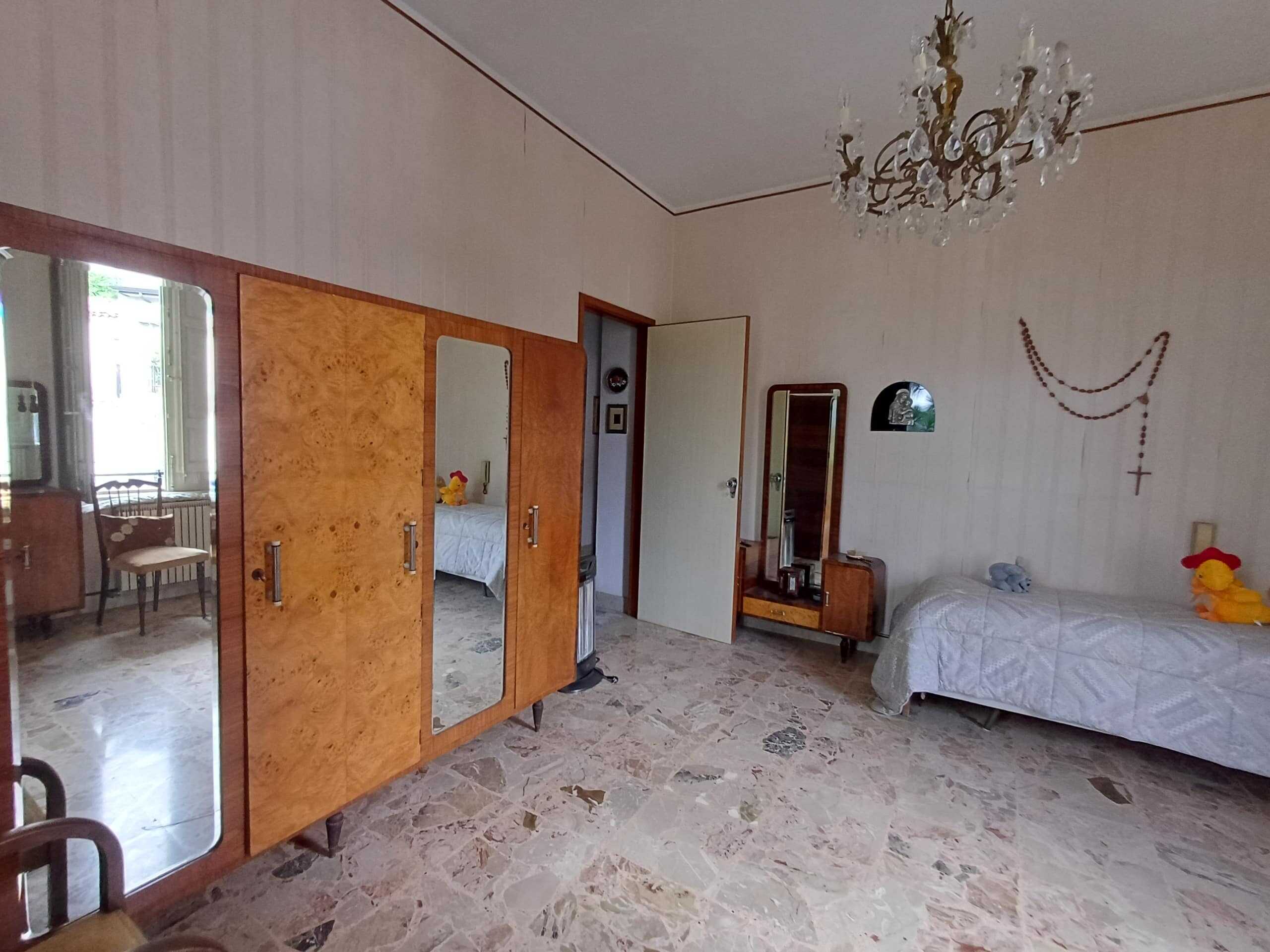 Antico camera da letto con armadio in stile vintage e decorazioni religiose, mobili in legno, pareti beige e pavimento in marmo, atmosfera classica e accogliente.