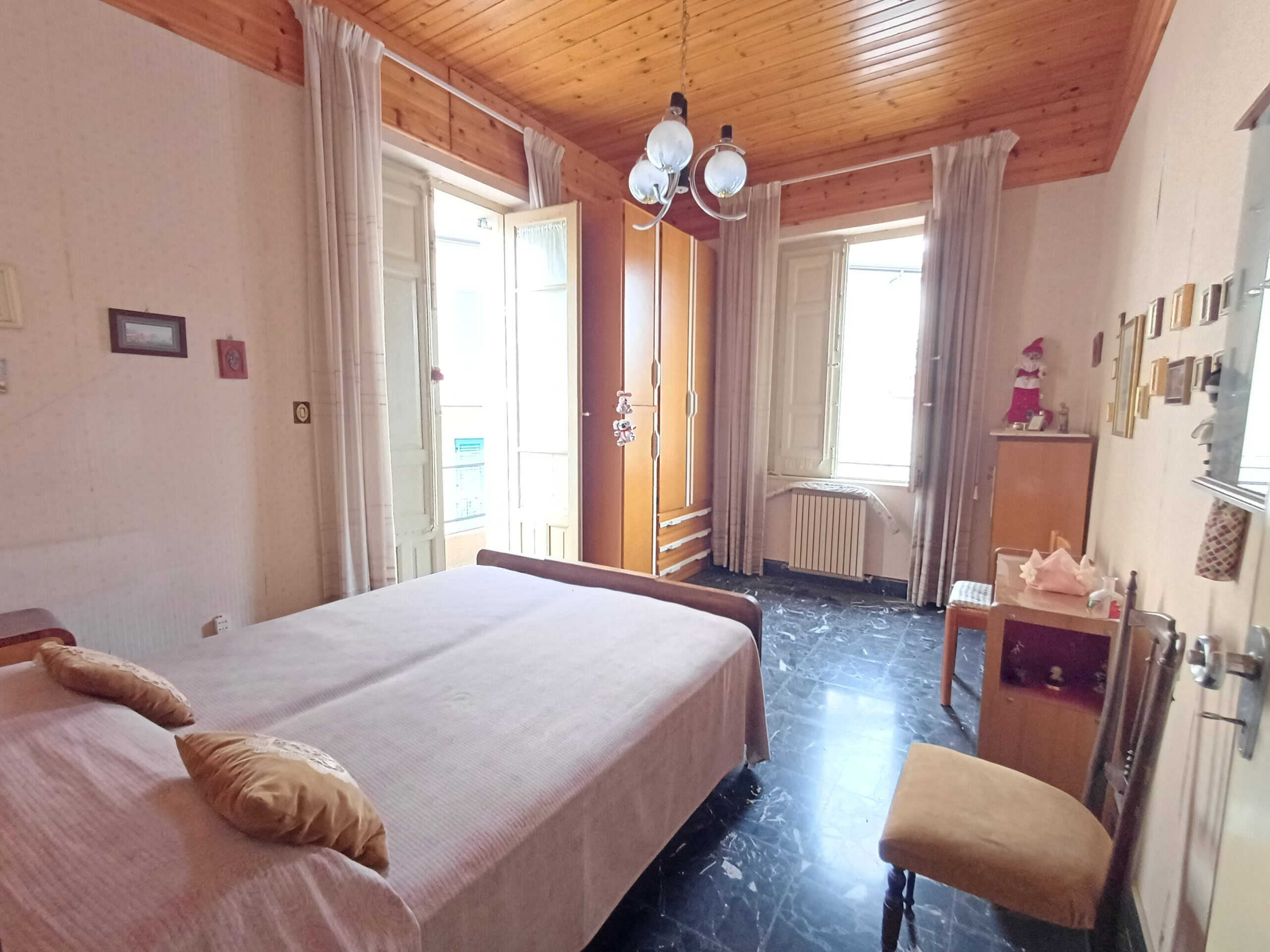 Camere da letto con finestre grandi e luce naturale, arredo classico, pavimento in marmo nero e soffitto in legno, ideale per case in vendita e affitti immobiliari.