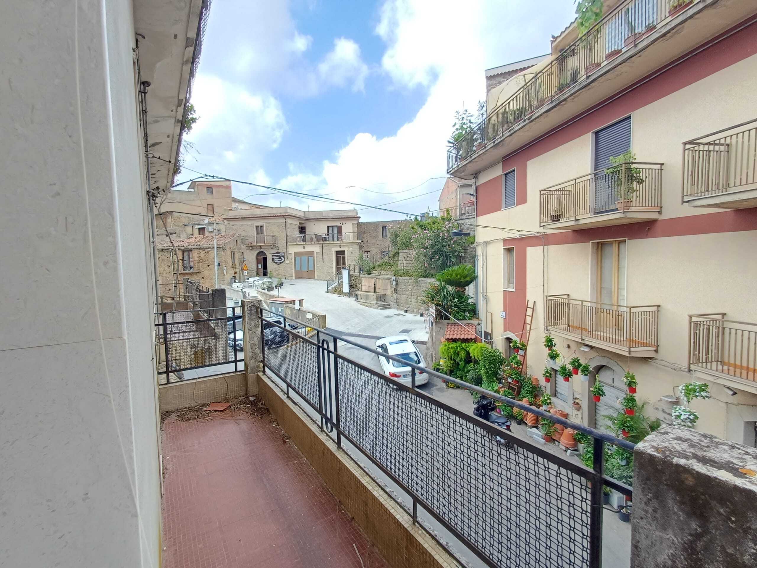 Balcone con vista su un angolo di strada nel centro storico di Matera, con edifici antichi, balconi fioriti e strada tranquilla, ideale per vivere l’atmosfera autentica della città.