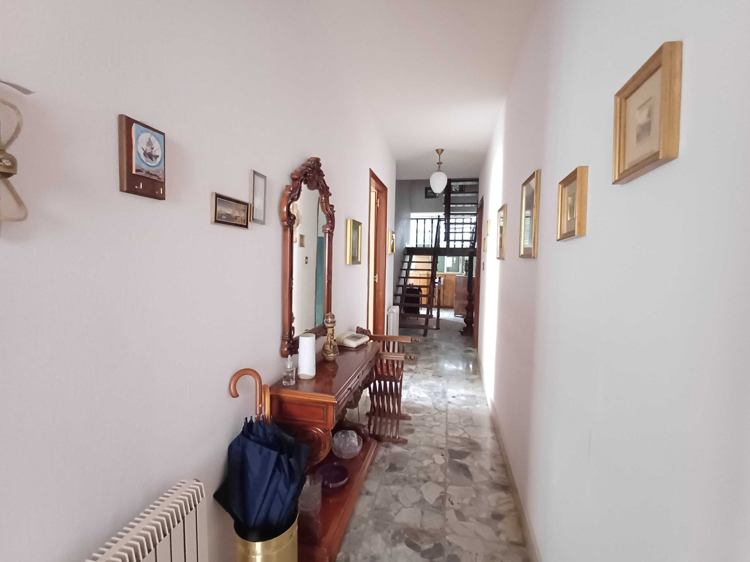 Elegante corridoio in appartamento con arredi in stile classico, specchio con cornice intagliata, pareti decorate con quadri e pavimento in marmo, ambiente luminoso e accogliente.