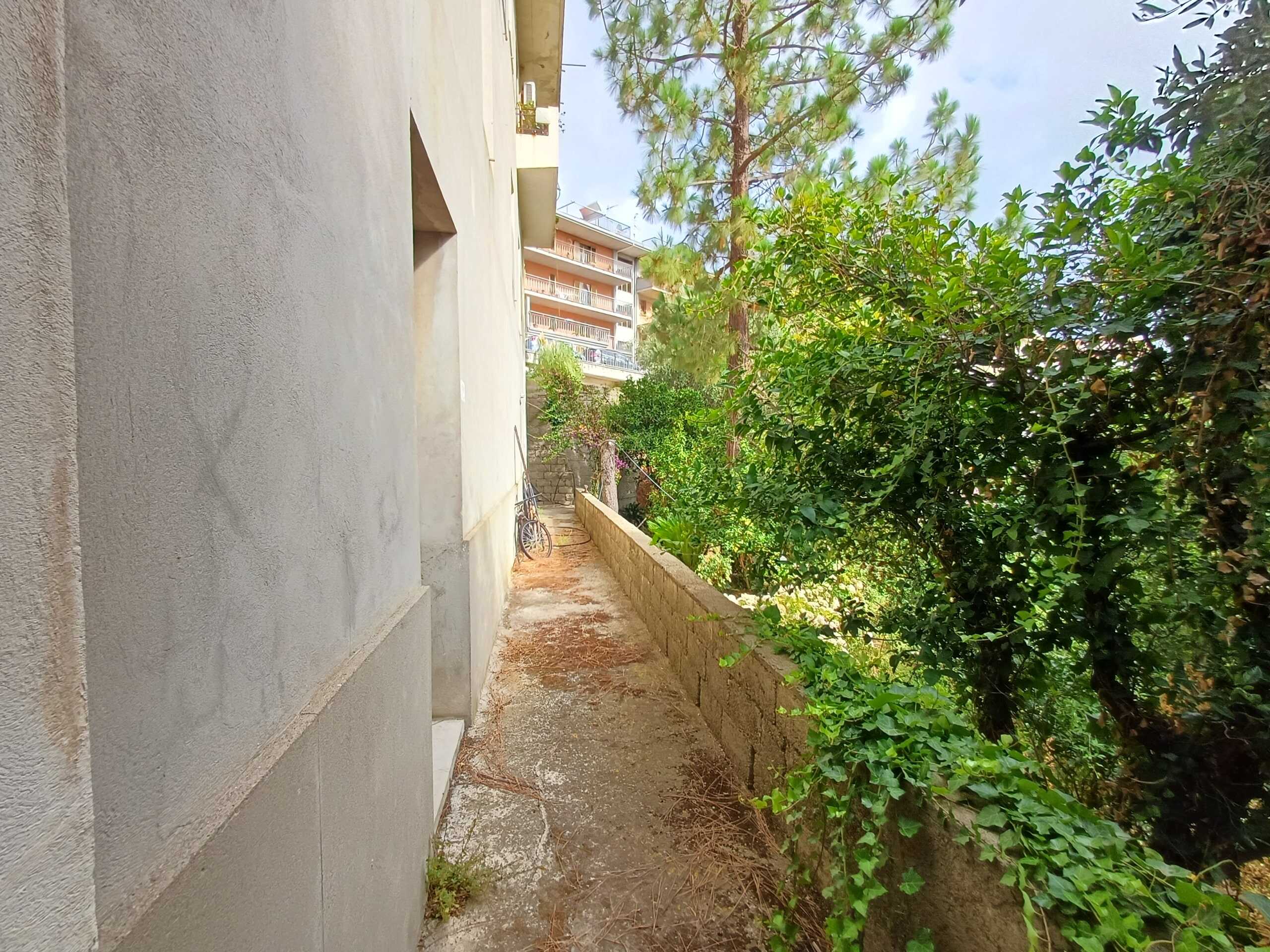 Sentiero esterno di una casa con muro di cemento e vegetazione lussureggiante, ideale per vivere in un ambiente tranquillo e naturale vicino alla città.