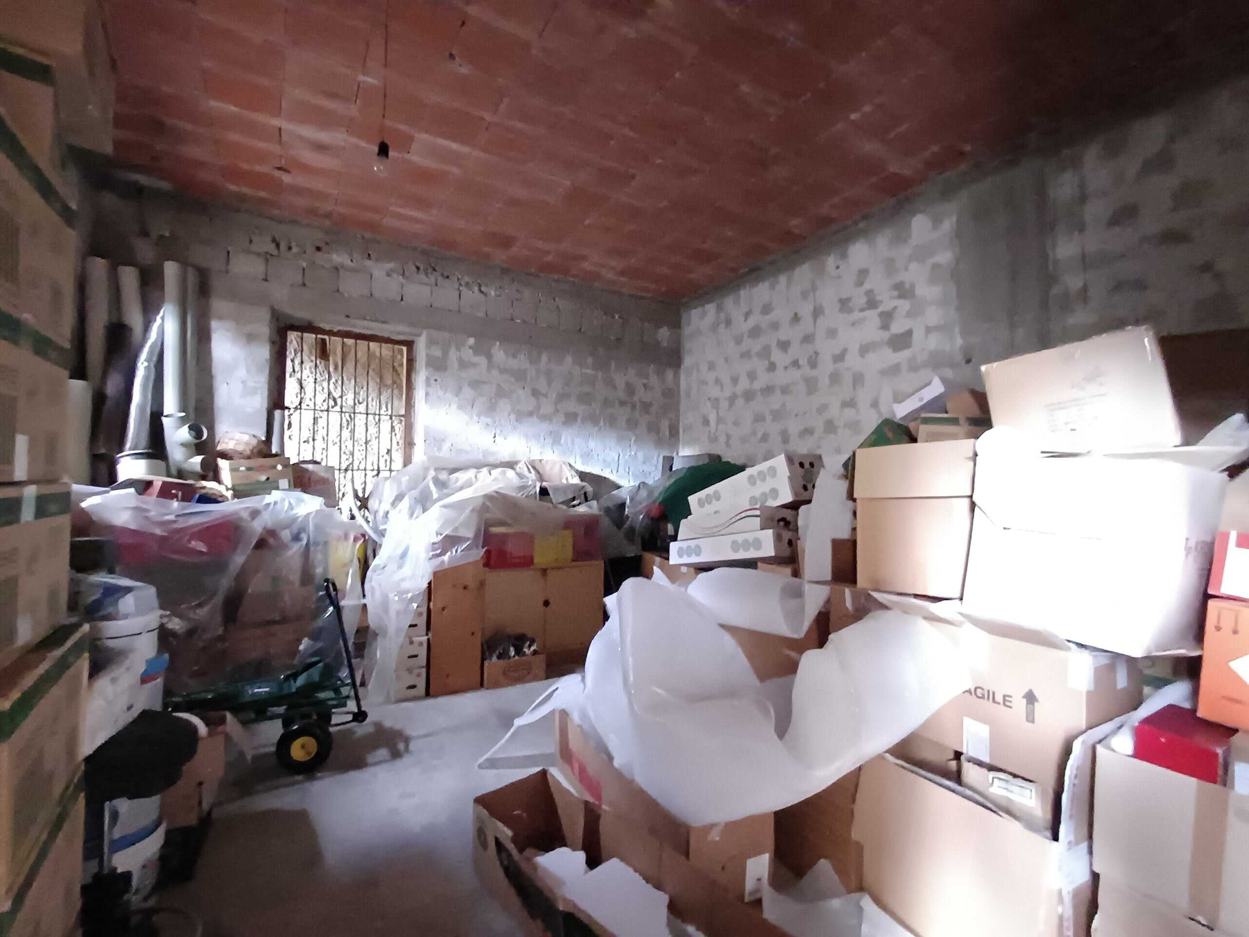 Scaffali e scatole di cartone in un garage o magazzino in fase di ristrutturazione o stoccaggio. Ambiente con muri in cemento e soffitto in legno, con luce naturale che entra da una finestra con grate.