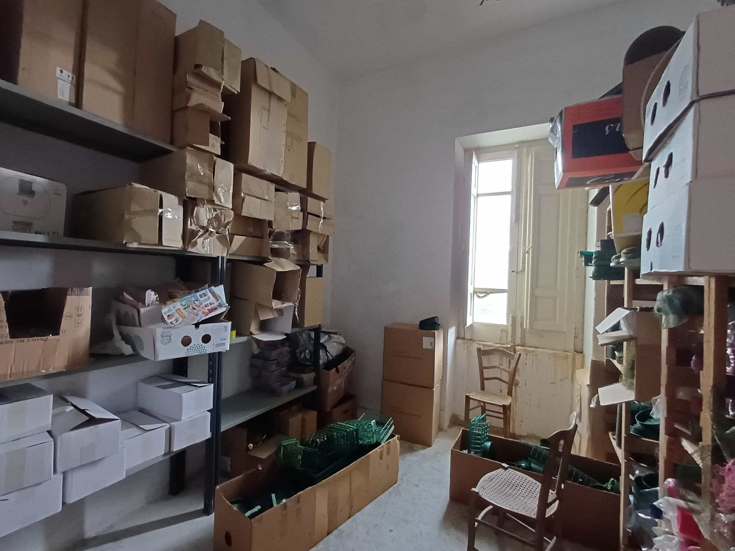 Scaffale pieno di scatole di cartone e materiali vari in una stanza con finestra, ambiente di magazzino o deposito.